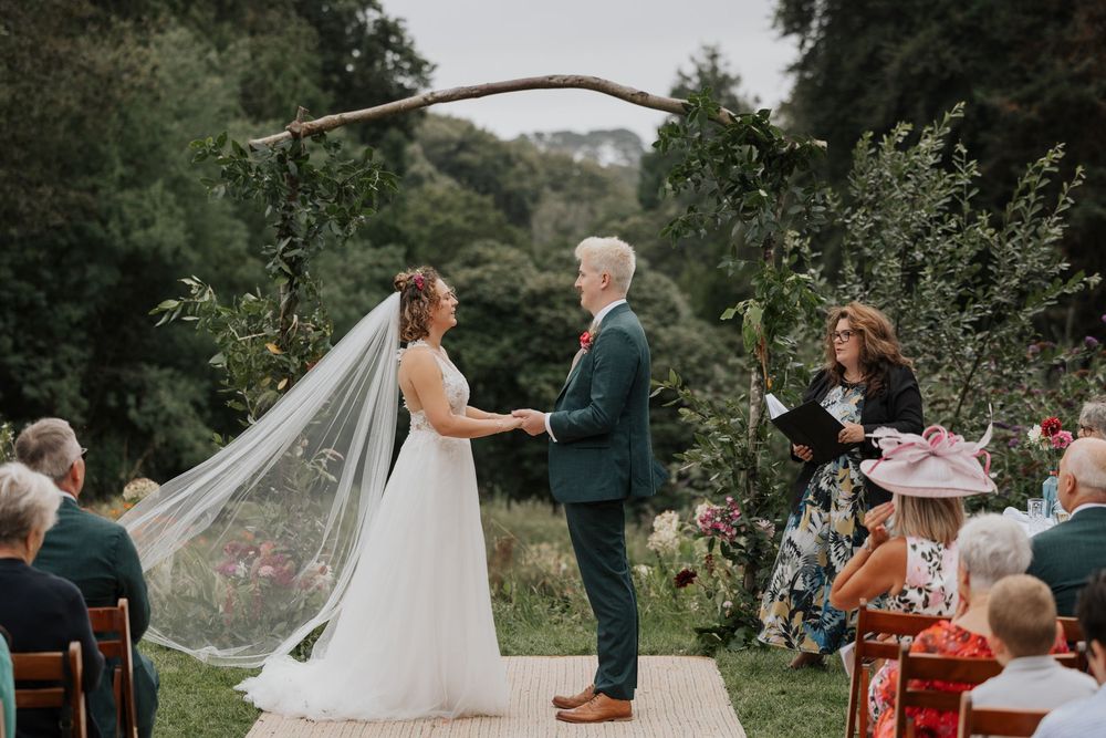 Bride and groom exchanging vows under a natural branch arch at an elegant outdoor garden wedding ceremony.