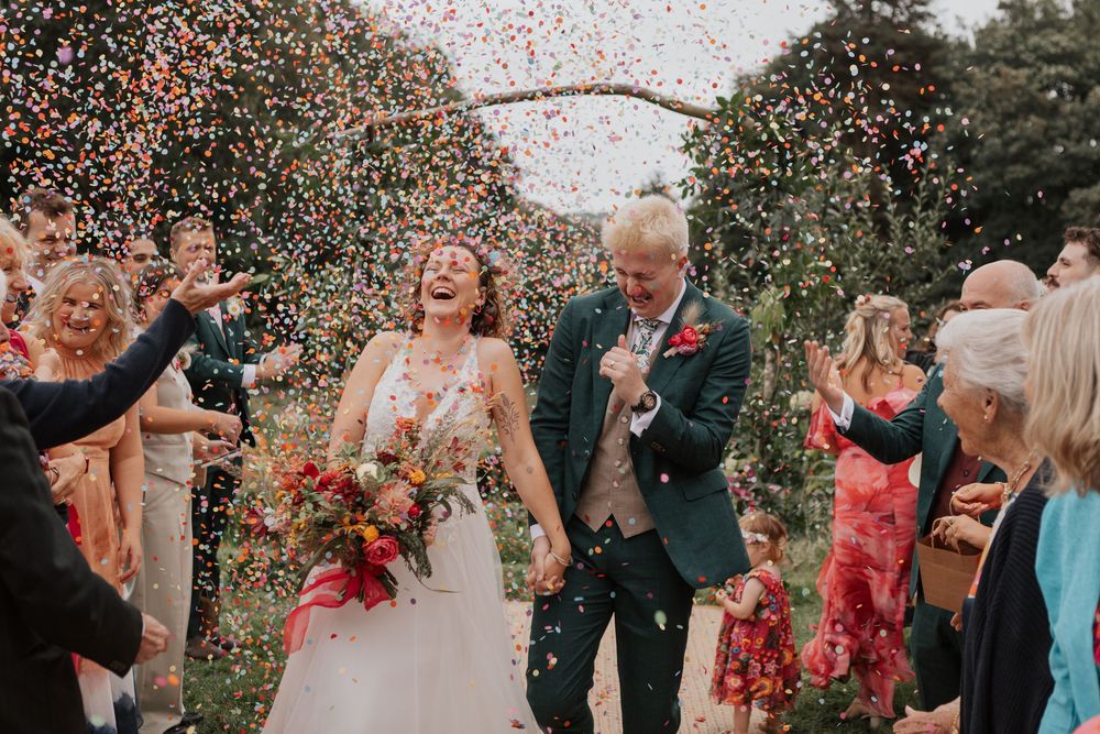 Newlyweds laughing as colorful confetti fills the air during joyful wedding celebration exit.