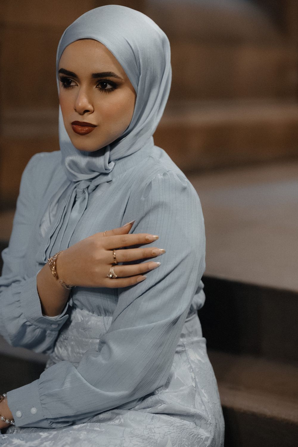 A sequence of portraits showing a person in a light blue hijab and white dress against a dark background.