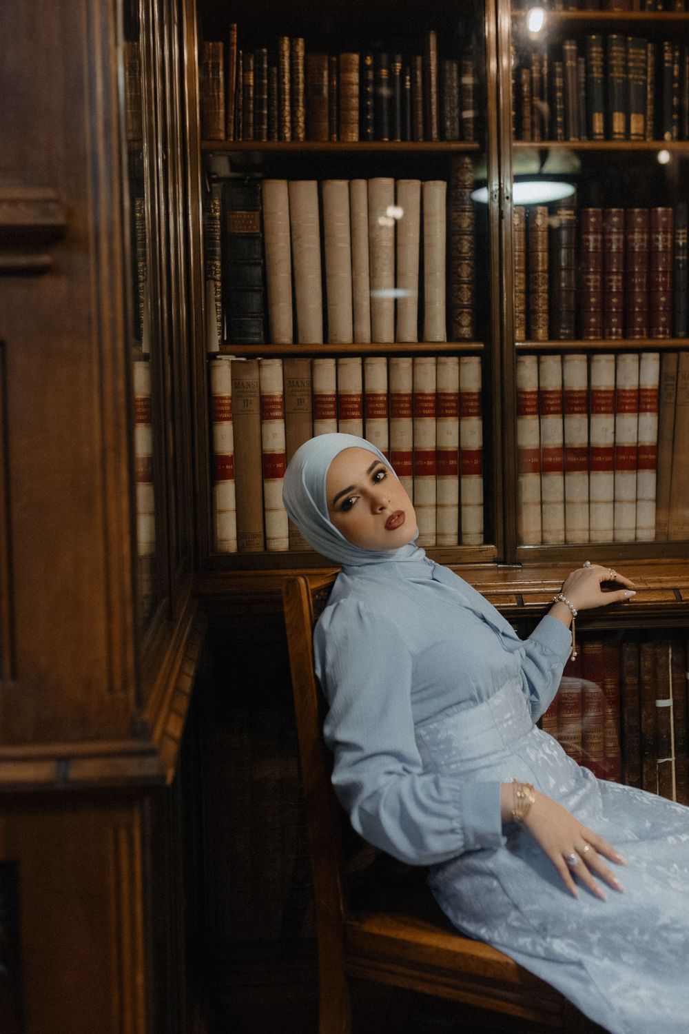 A photo series in a library showing someone in blue clothing posing dramatically among wooden bookshelves.