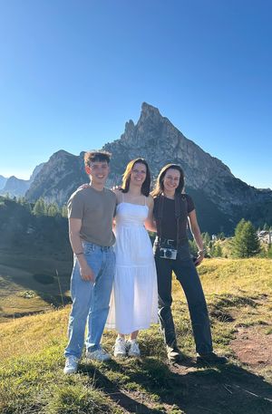 A group poses against a stunning mountain backdrop in the Dolomites on a sunny day with clear blue skies.