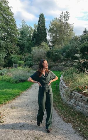 A person in dark clothing strikes playful poses along a gravel path bordered by stone walls and trees.