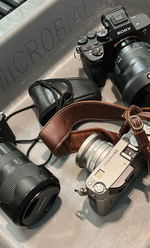 Digital and film cameras with leather straps sit side by side on a light gray surface at airport security.