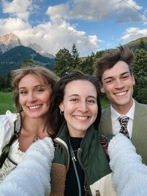 A selfie of a photographer with a freshly married couple together outdoors with mountains and cloudy skies visible in the background.