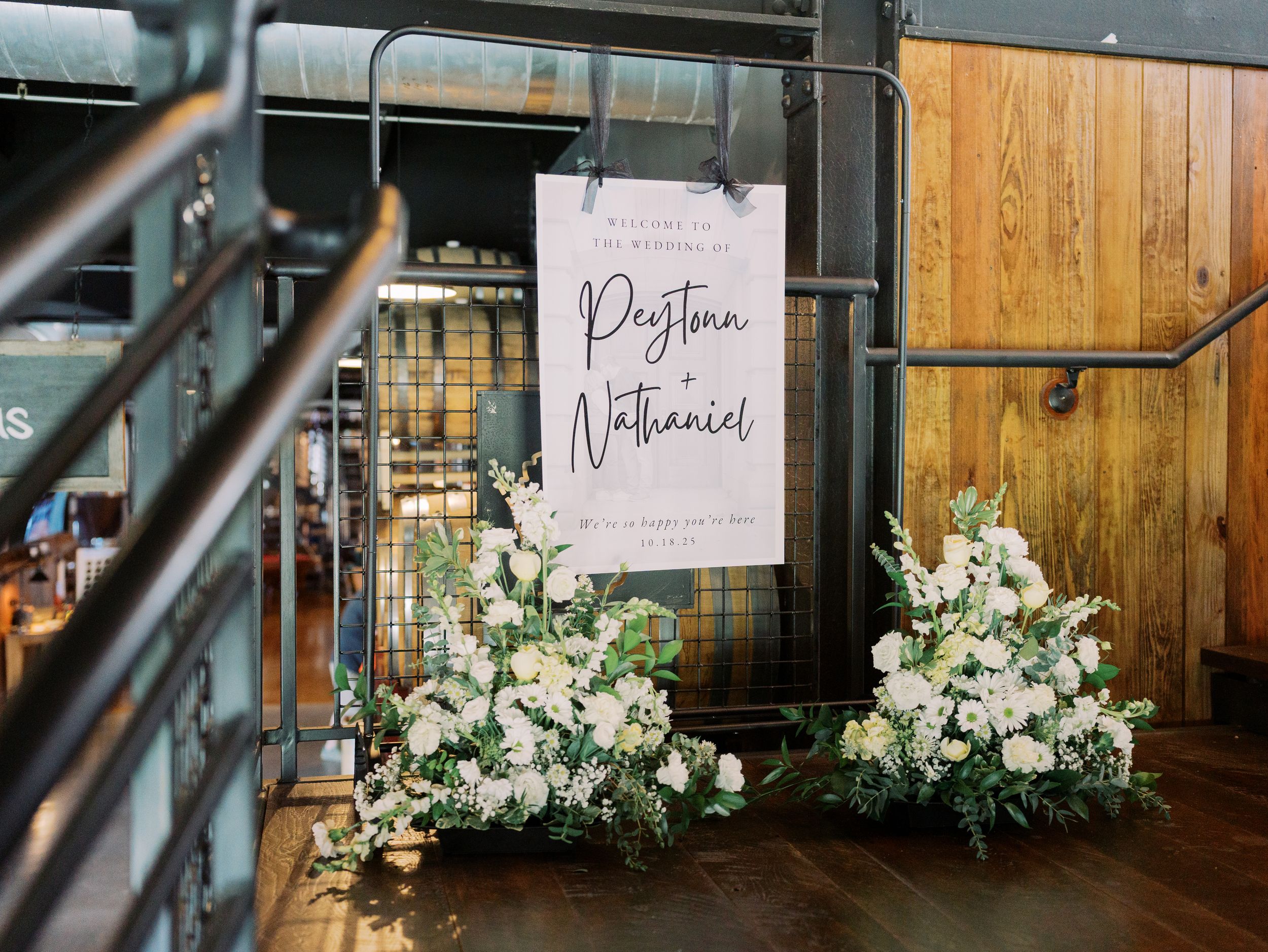 White floral arrangements line a rustic wooden wall in an industrial-style event venue.