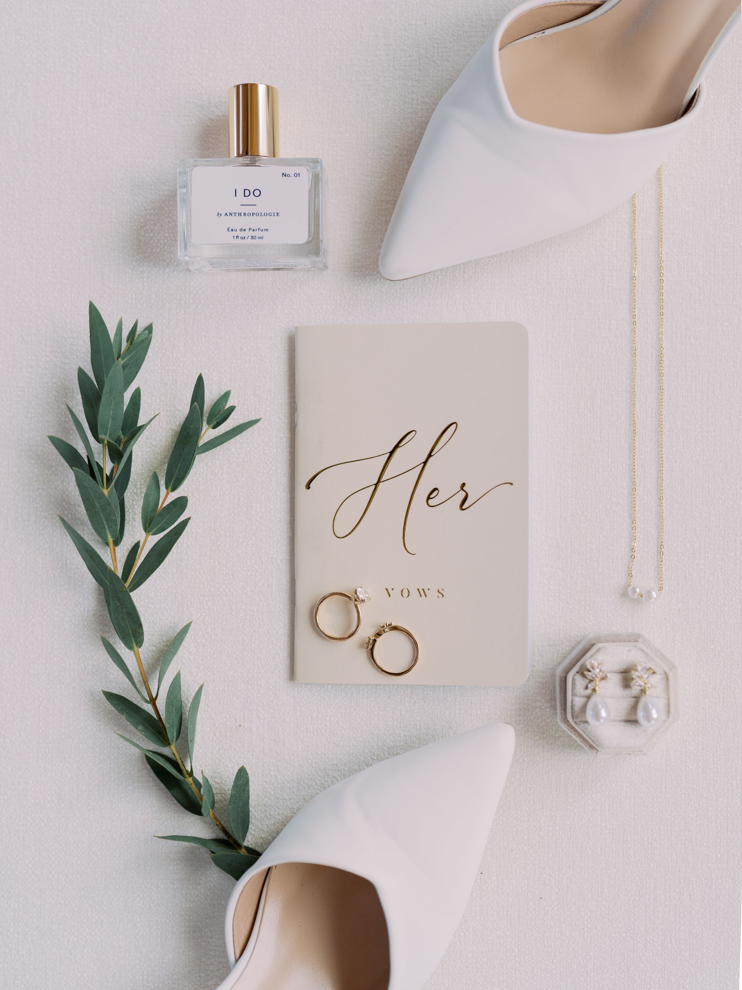 Minimalist wedding flat lay with olive branches, rings, and white paper details on light gray background.
