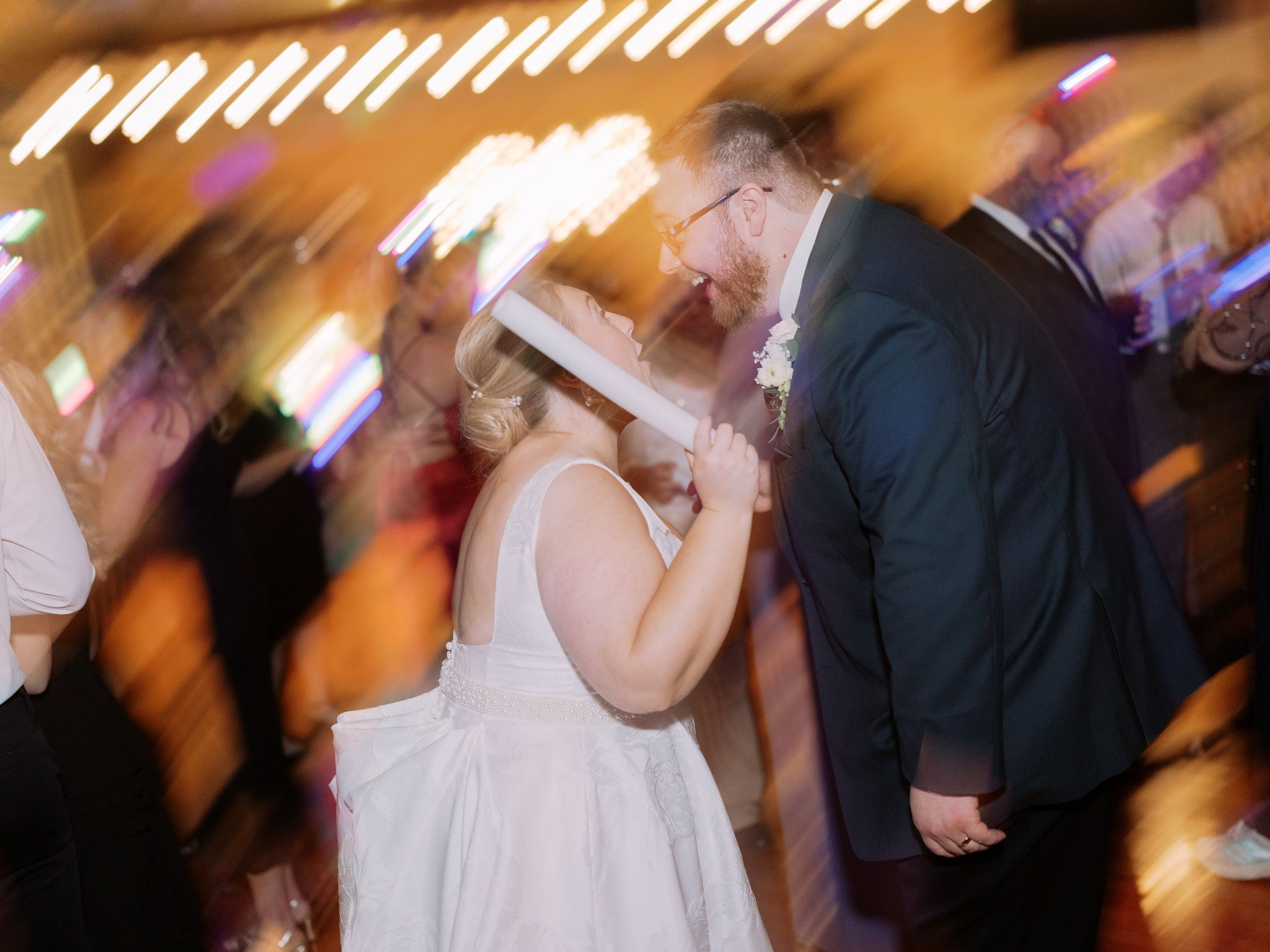 Motion-blurred wedding reception dance floor with glowing lights and silhouettes of people dancing and celebrating.