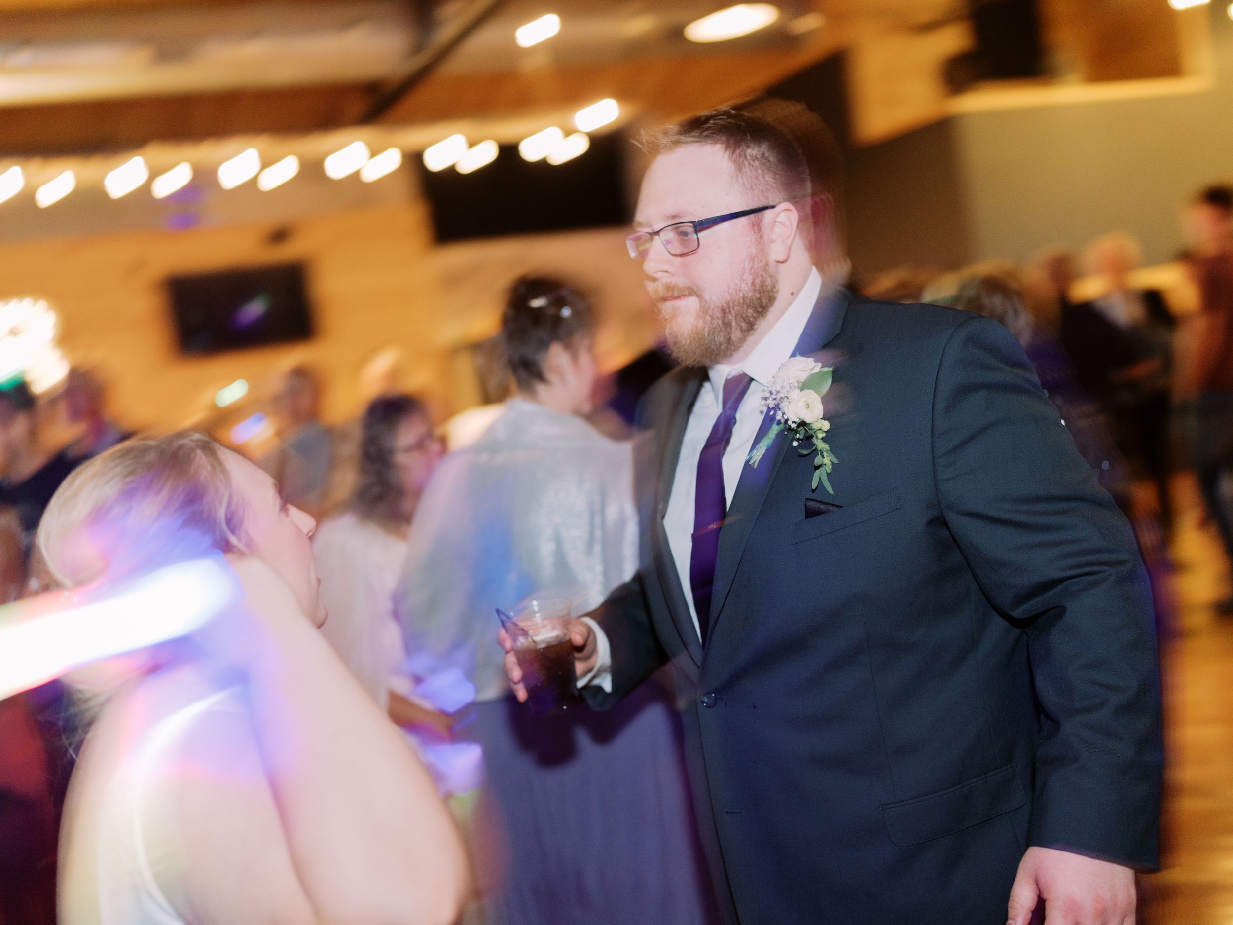 Guests dance and celebrate at an indoor wedding reception with string lights and warm lighting.