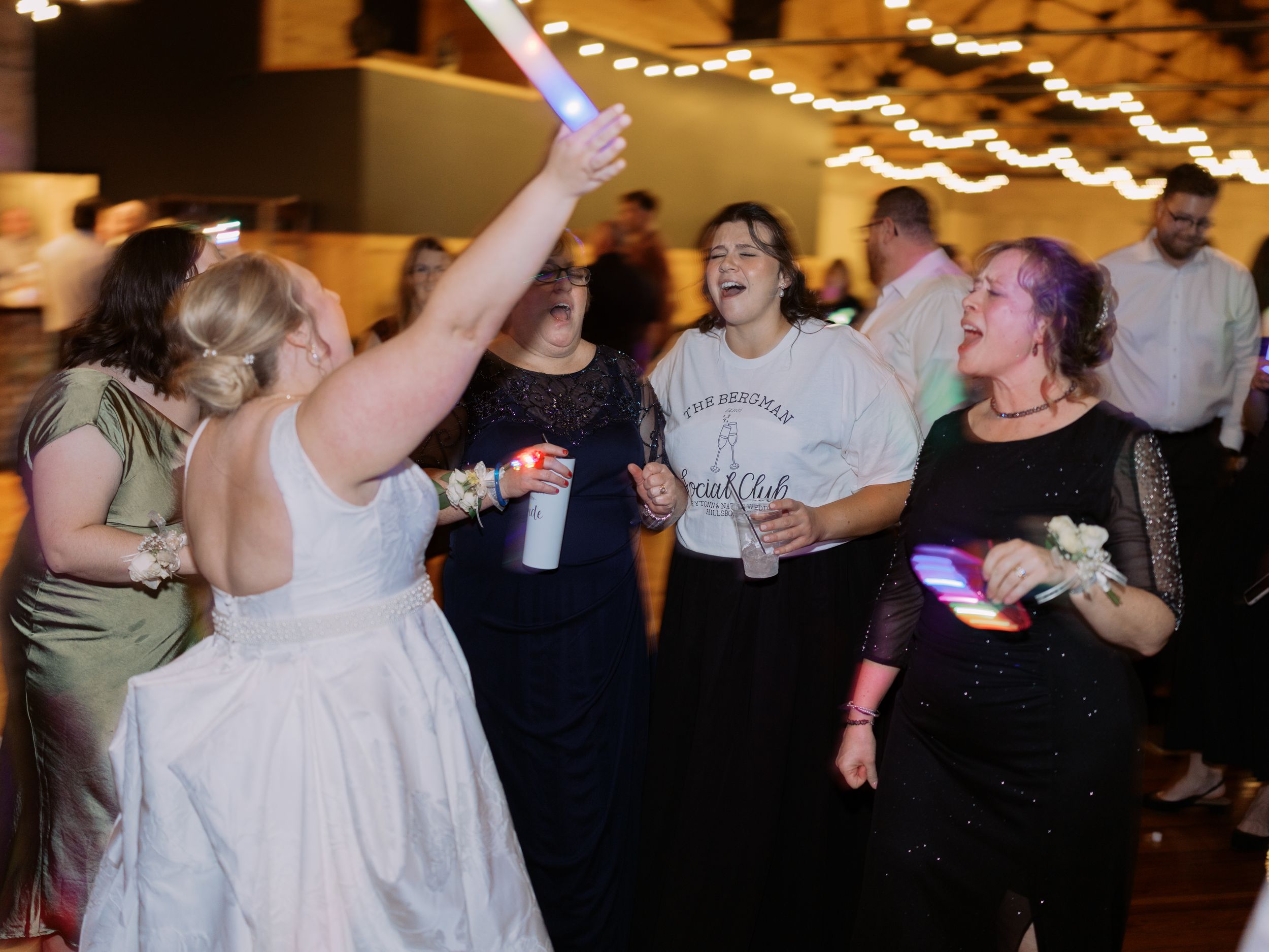People dancing and celebrating at a lively indoor event with string lights decorating the ceiling.