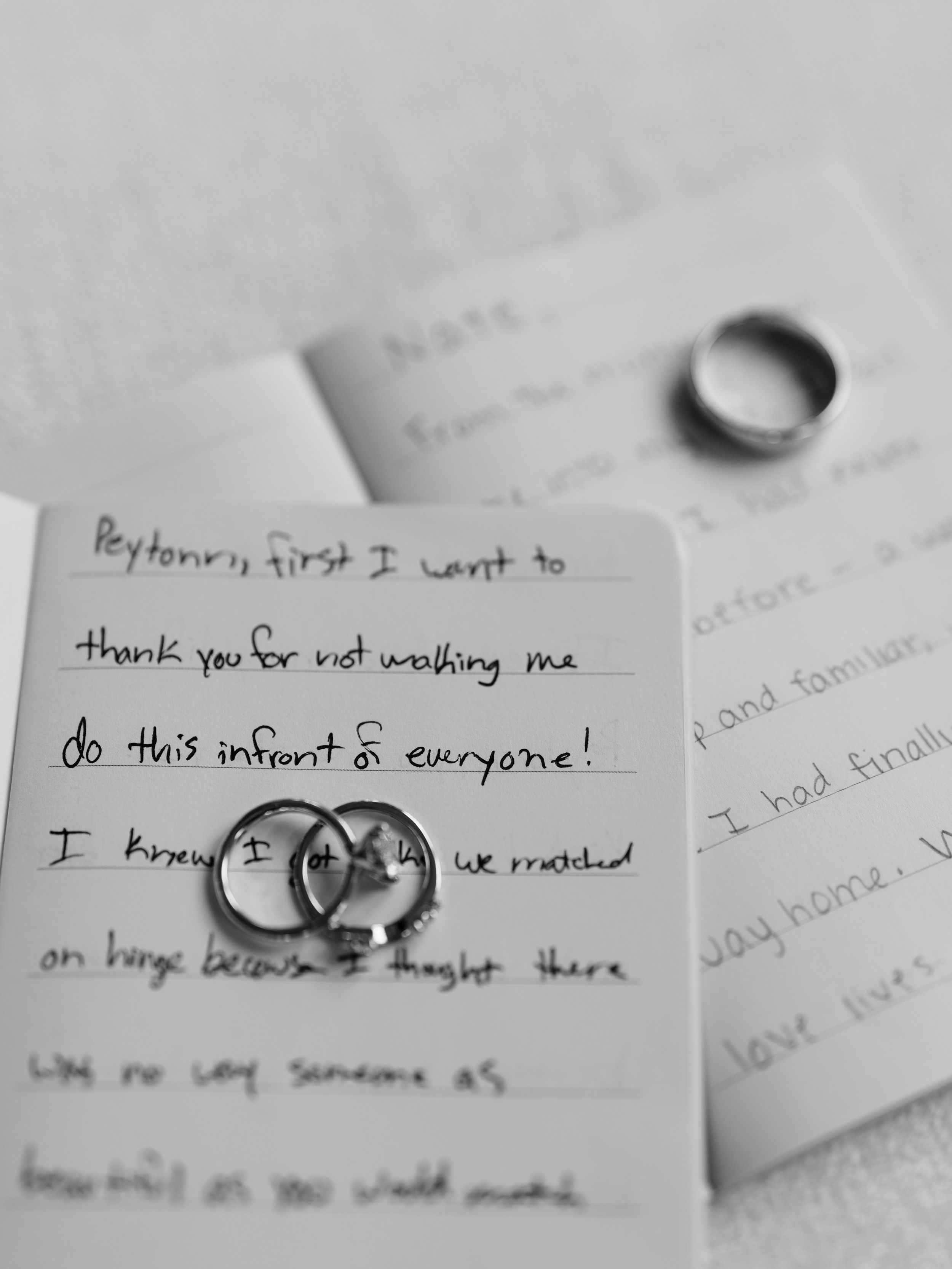 Black and white photo of wedding rings and a handwritten note on paper creating a romantic composition.