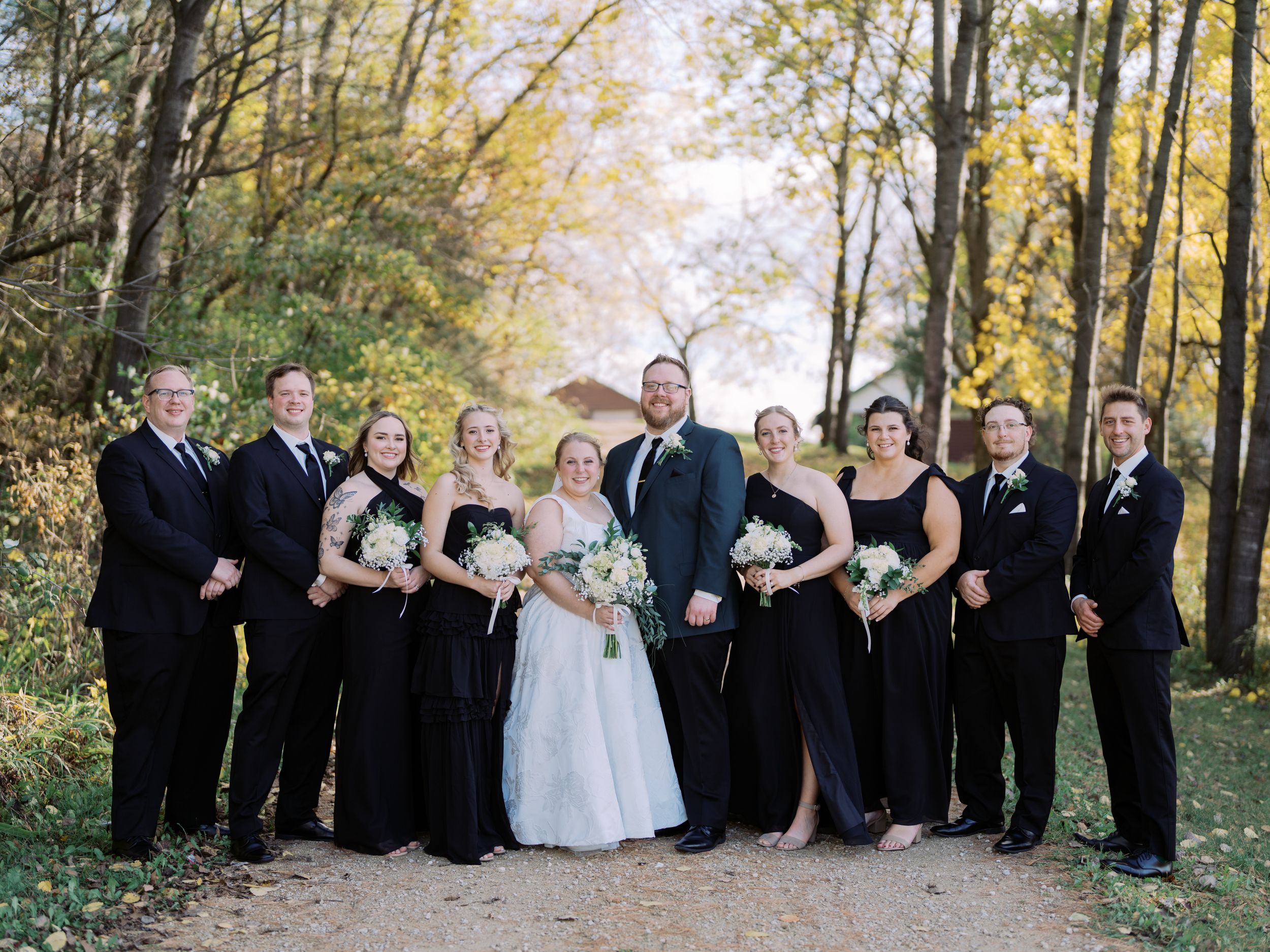 Wedding party poses together outdoors during autumn with golden trees and falling leaves in the background.