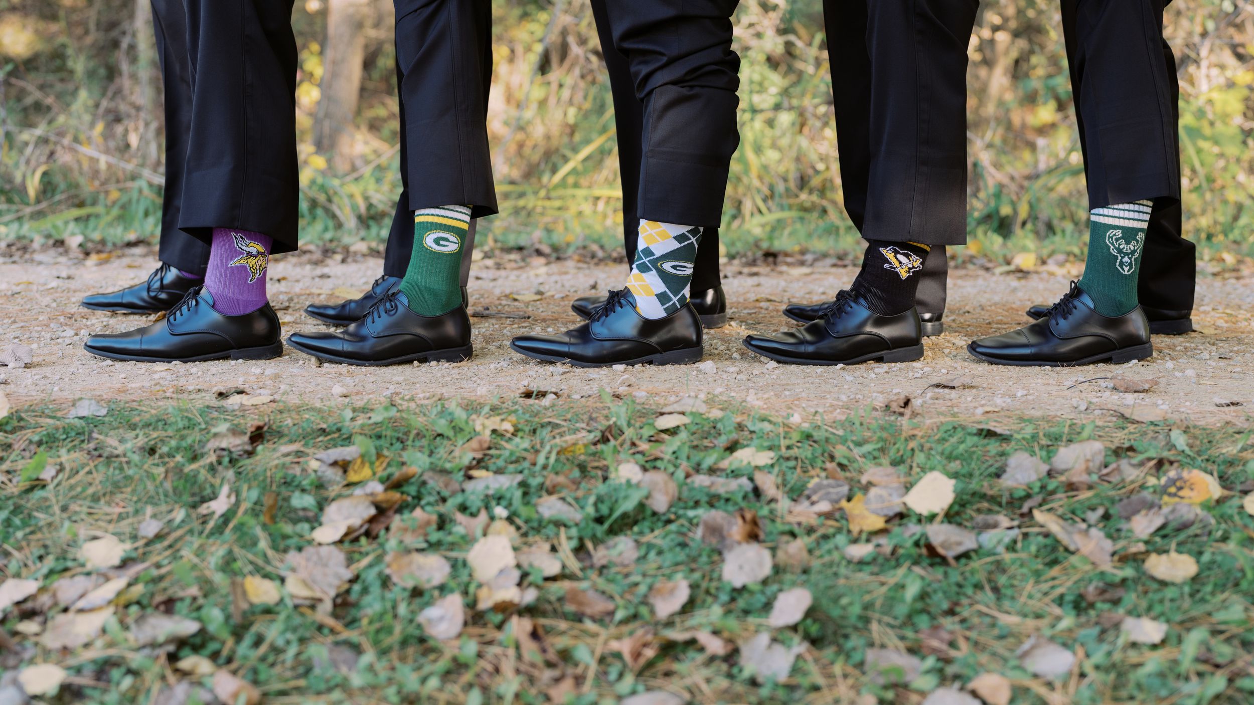 Feet of people walking on fallen autumn leaves scattered along a garden path.