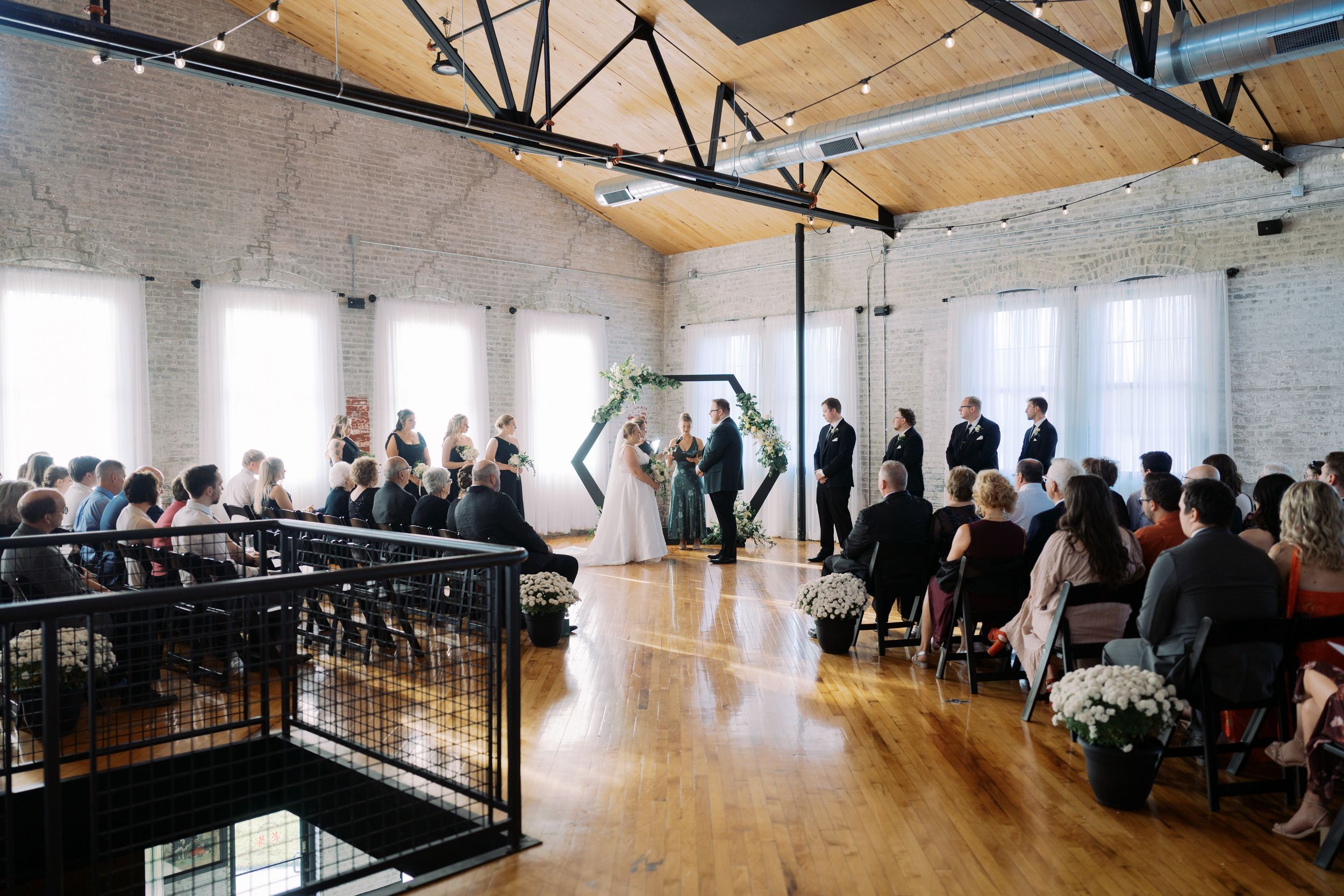 A panoramic view of a modern wedding venue with exposed beams, white walls and guests seated along the perimeter.