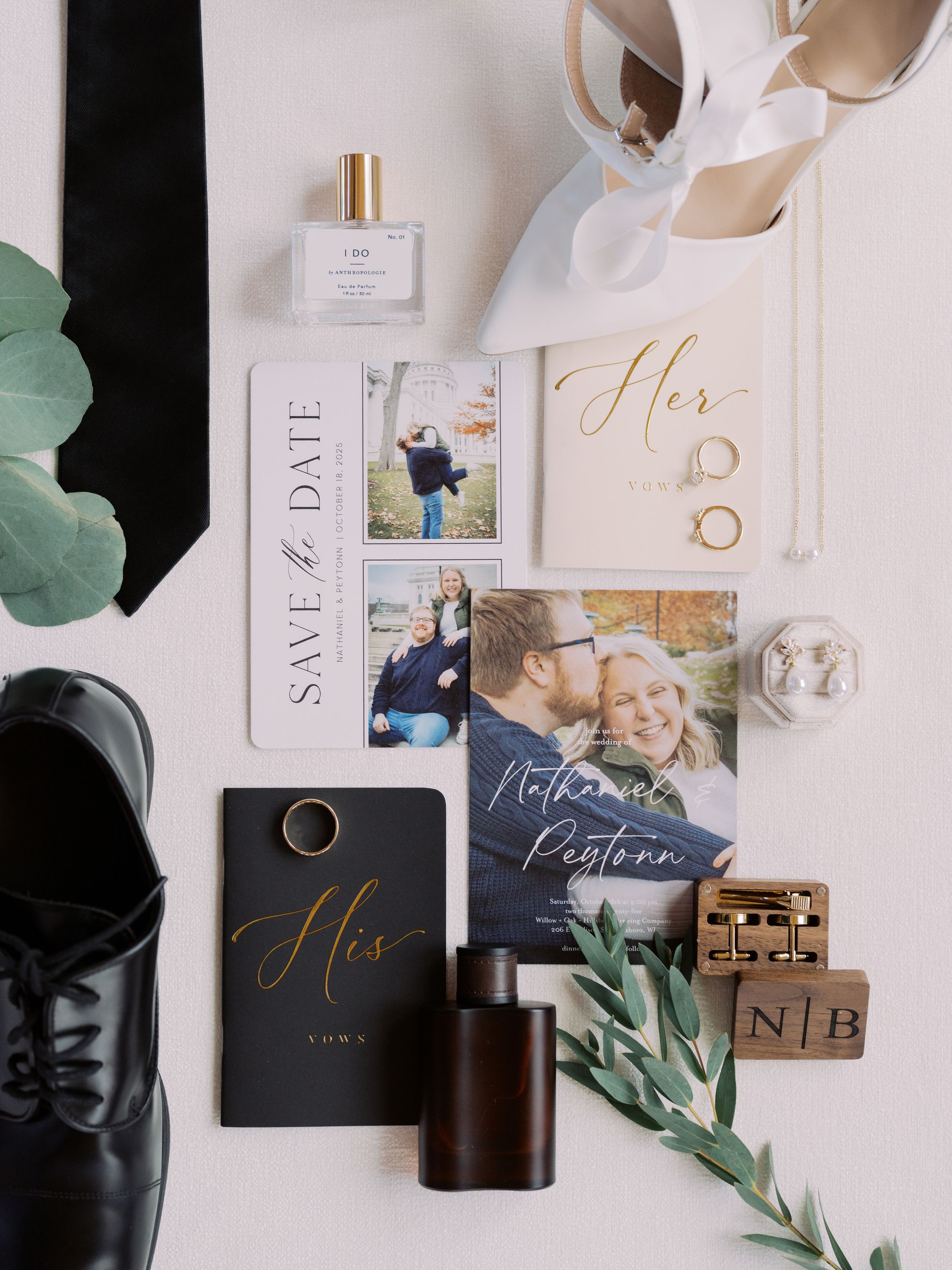 Wedding stationery flatlay with elegant invitations, rings, and eucalyptus leaves on a white background.