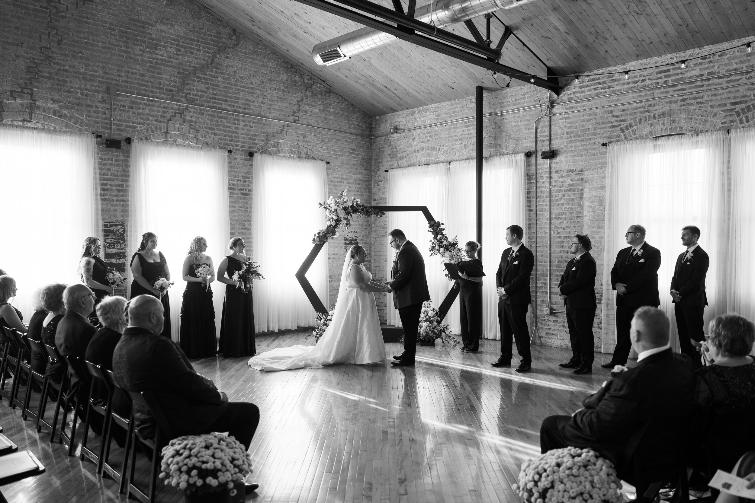 A series of black and white wedding ceremony photos showing a gathering in an indoor venue with natural light.