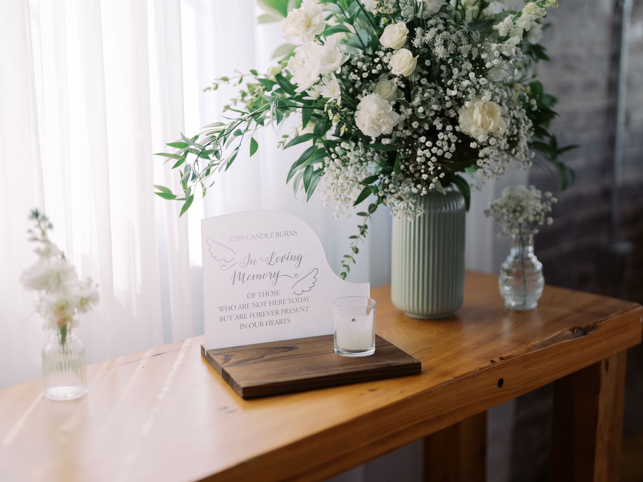 White floral arrangements in small vases line a wooden table with delicate greenery and decorative elements.