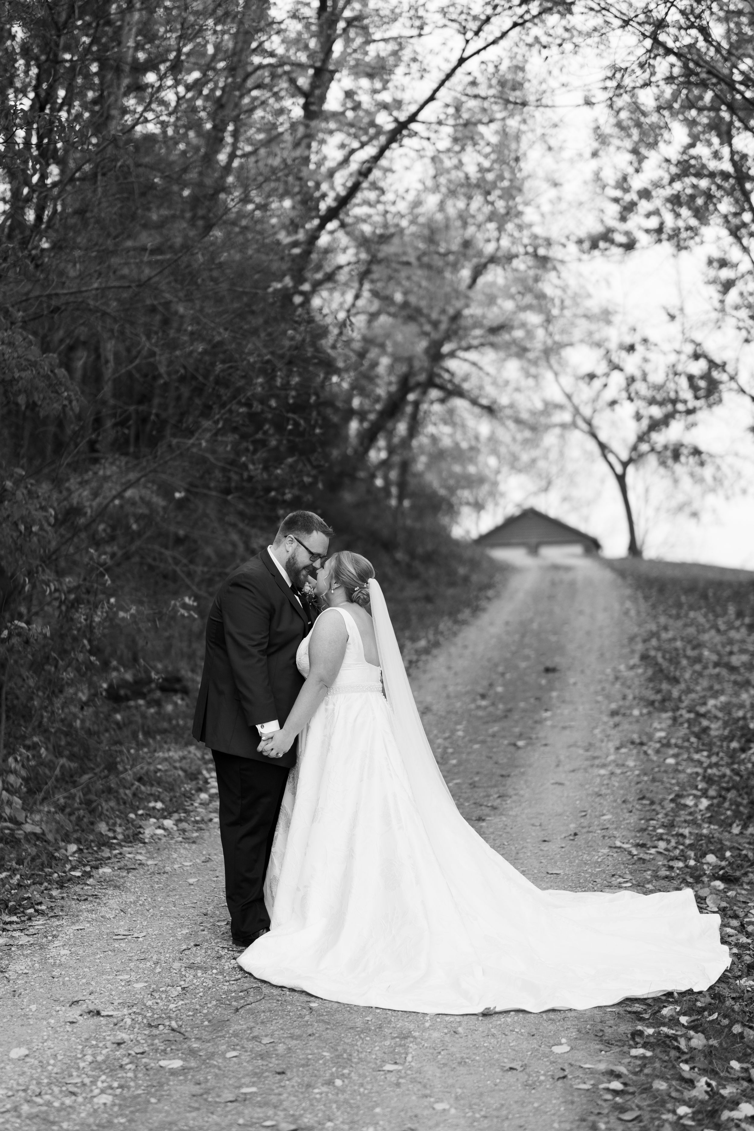 A romantic black and white wedding photo series showing a couple on a tree-lined path with fallen autumn leaves.