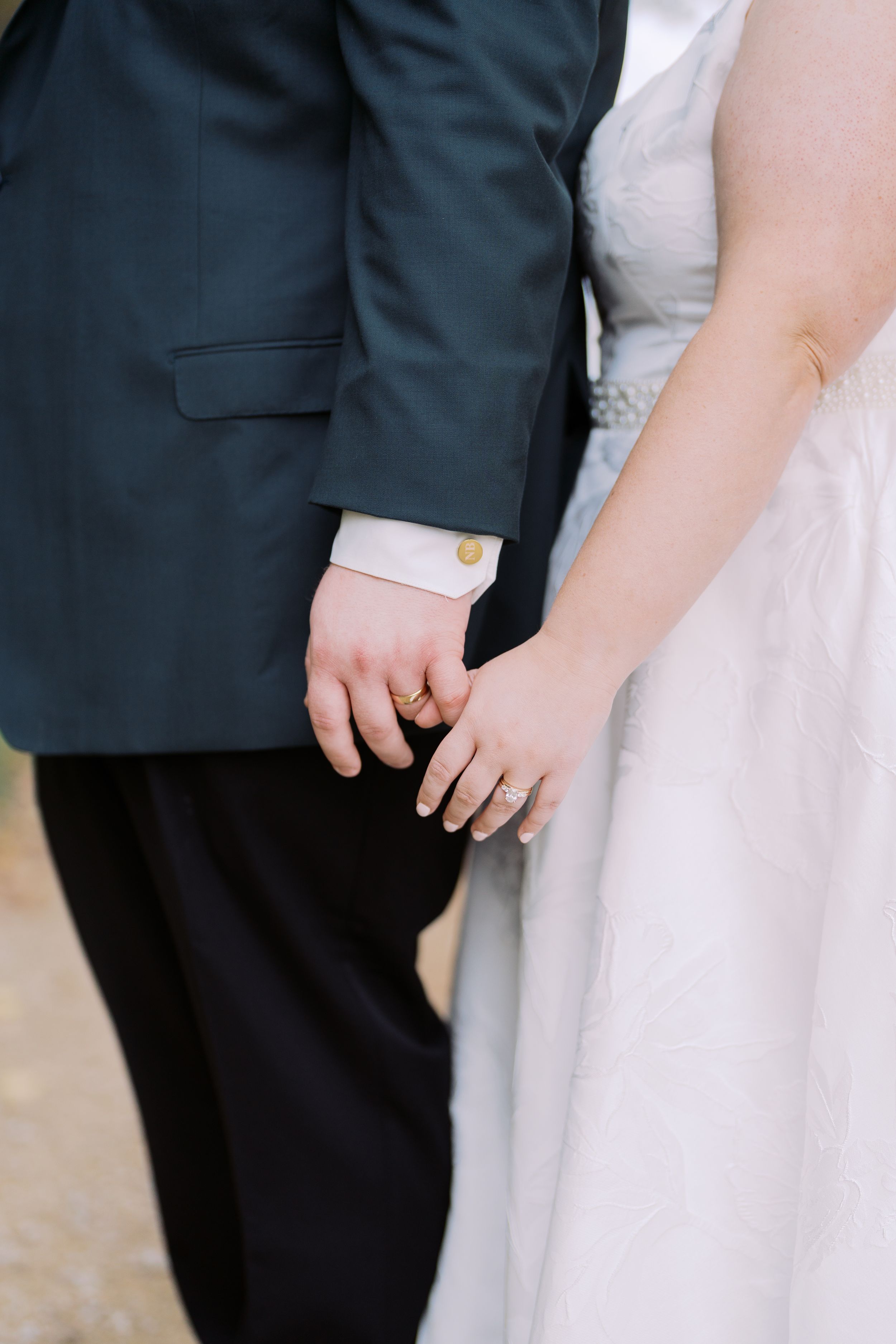 Close-up of bride and groom holding hands, showing wedding attire with dark suit jacket and white dress.