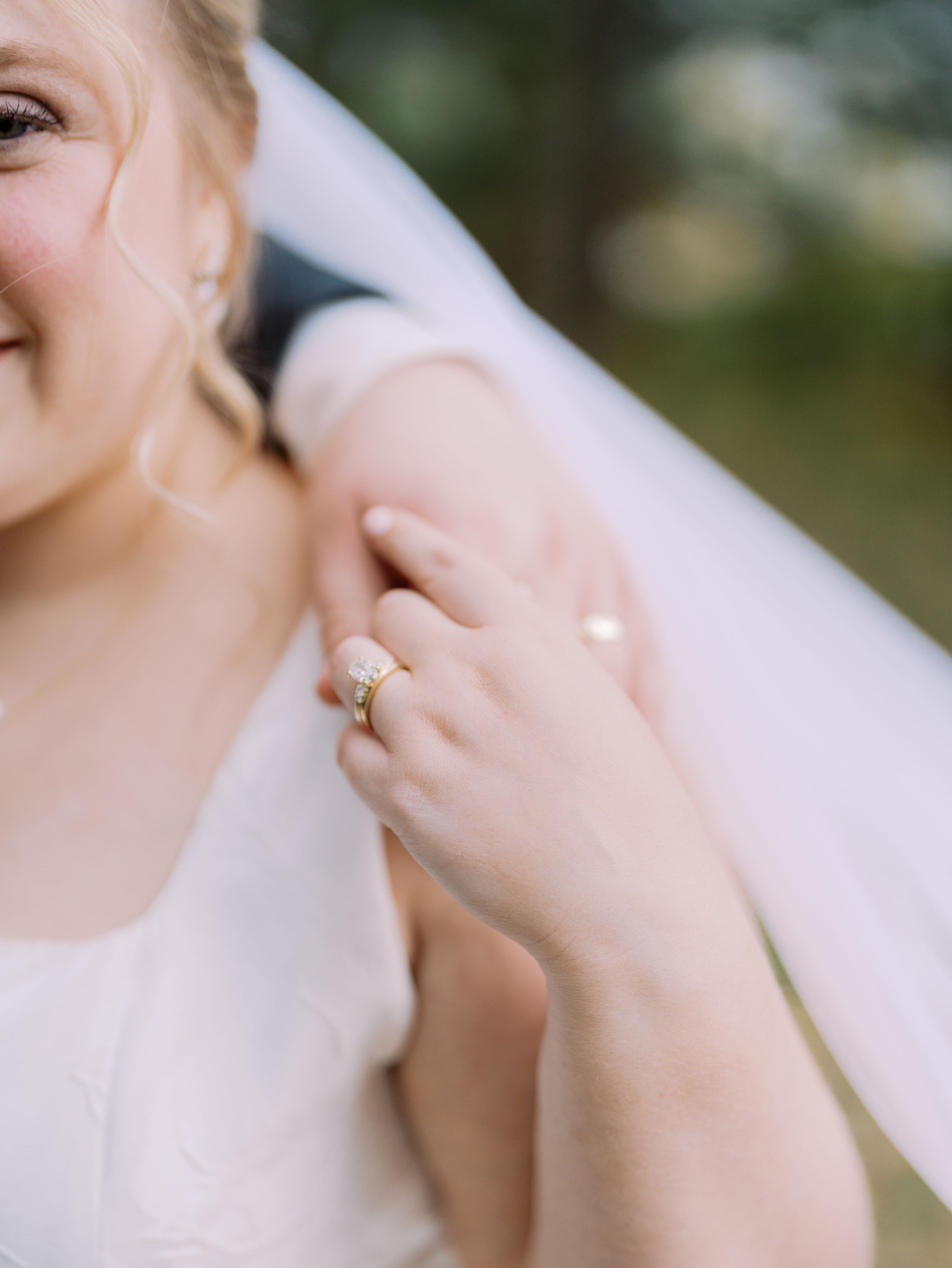 Close-up view of a delicate engagement ring with sparkling diamond on a woman's hand against a soft blurred background.