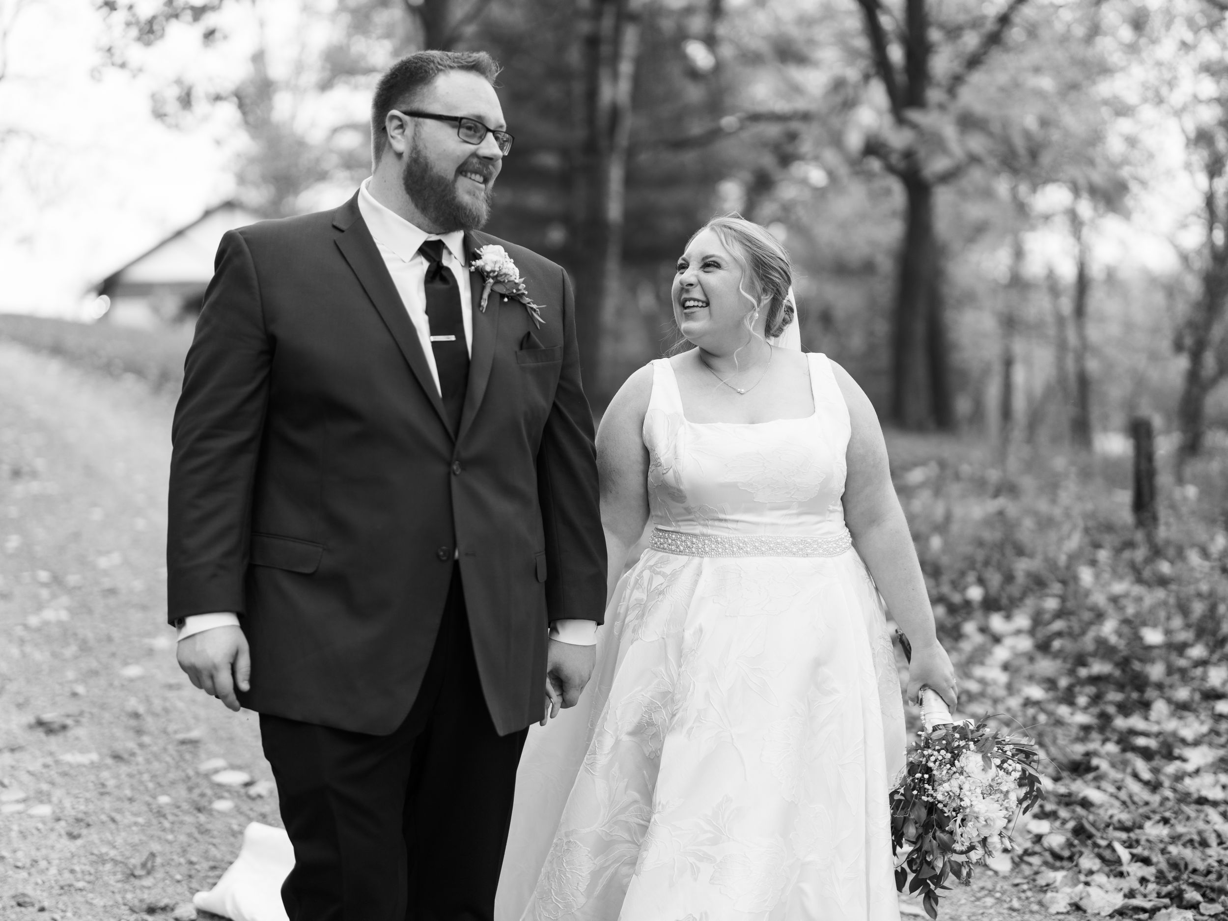 A happy couple shares joyful laughter together during an outdoor autumn photo session in black and white.