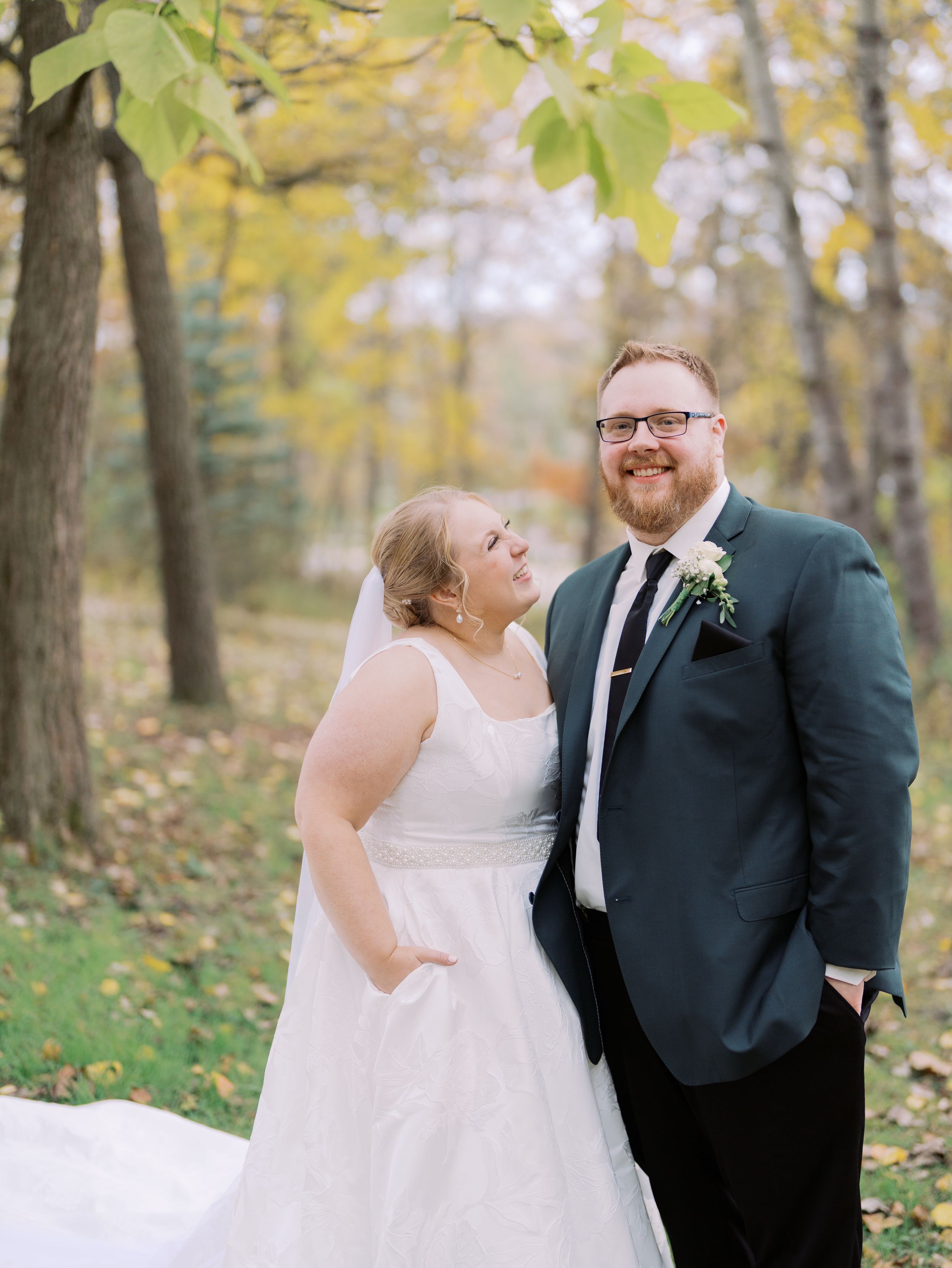 A joyful wedding couple shares a candid moment together in an autumn forest setting with yellow foliage.