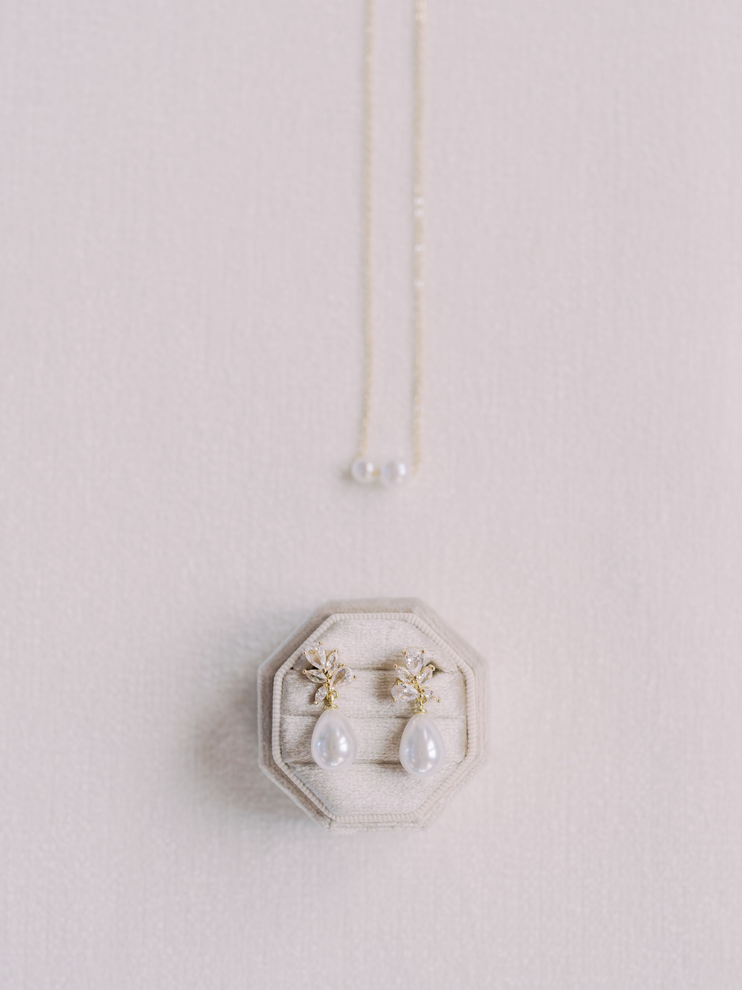 Delicate gold and pearl hexagonal stud earrings displayed on a white surface in a minimalist composition.