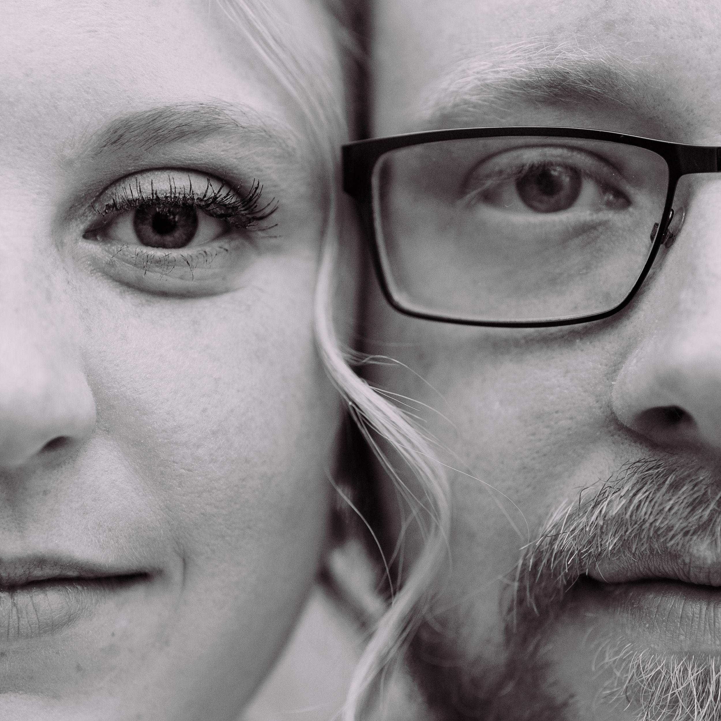 A black and white close-up portrait showing half faces of two people, one wearing glasses, positioned side by side.