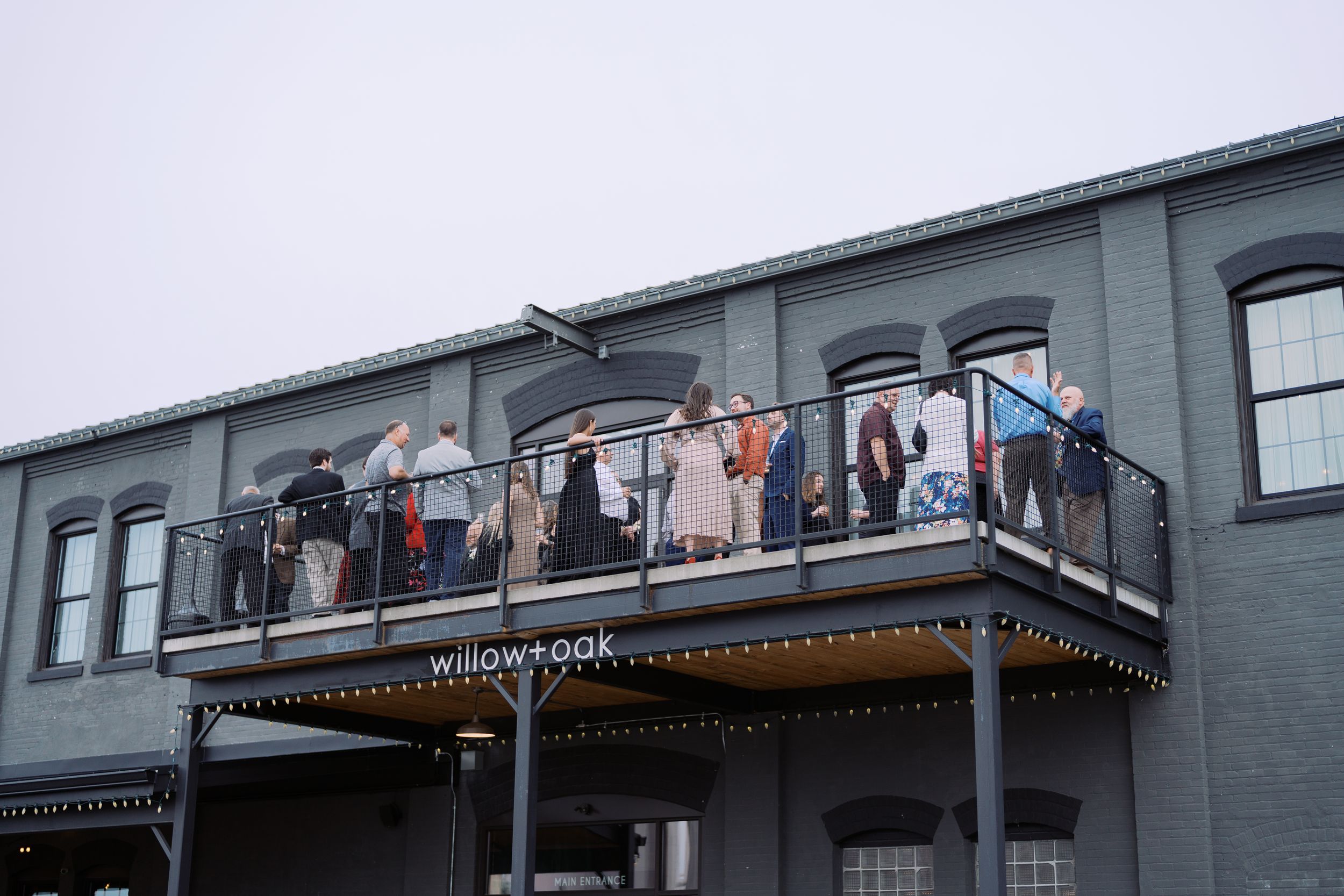 People gather on a balcony of a gray building during what appears to be a social event or celebration.