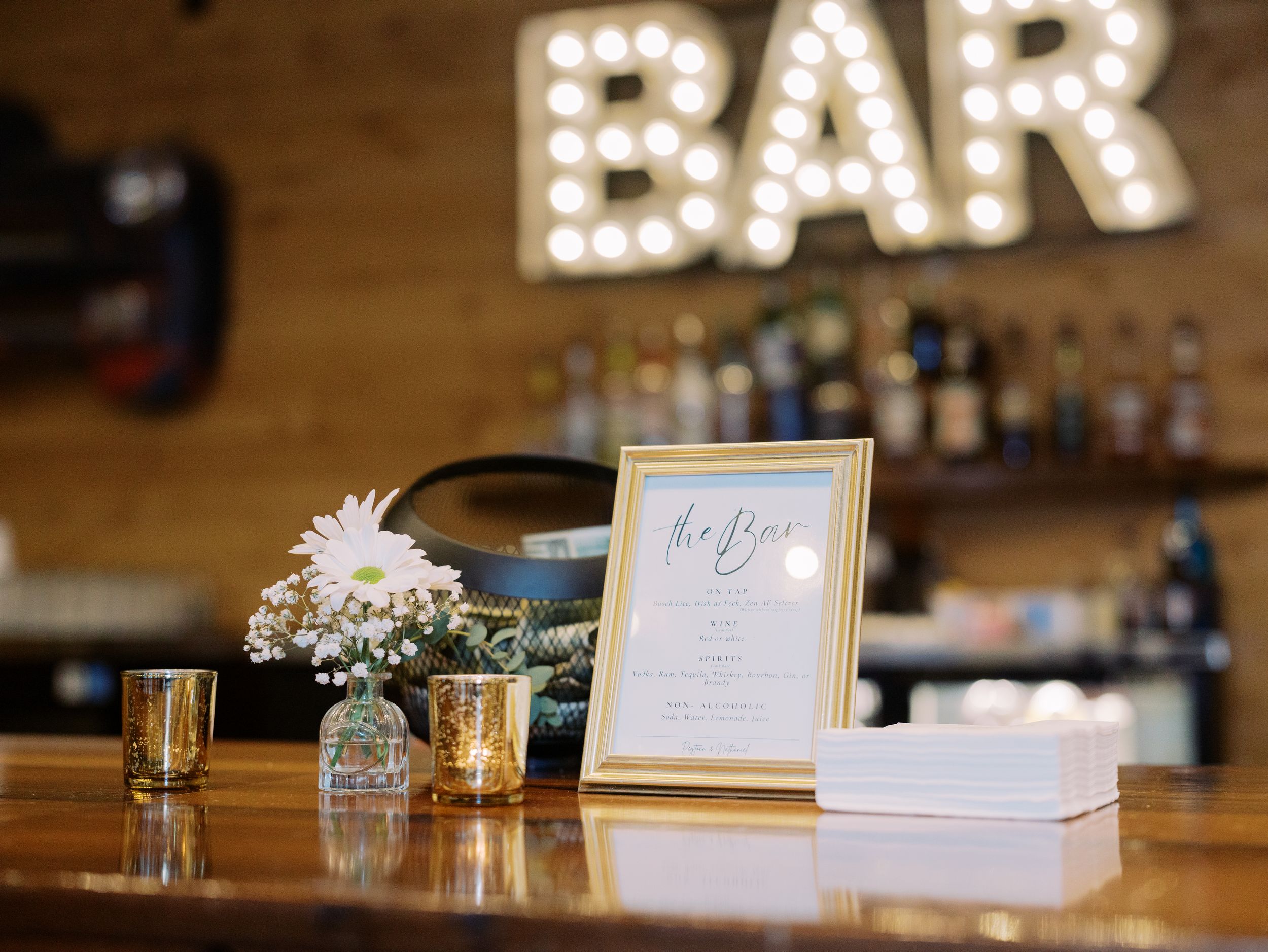 Illuminated 'BAR' sign with decorative lights glows warmly against a rustic wooden wall in a restaurant setting.