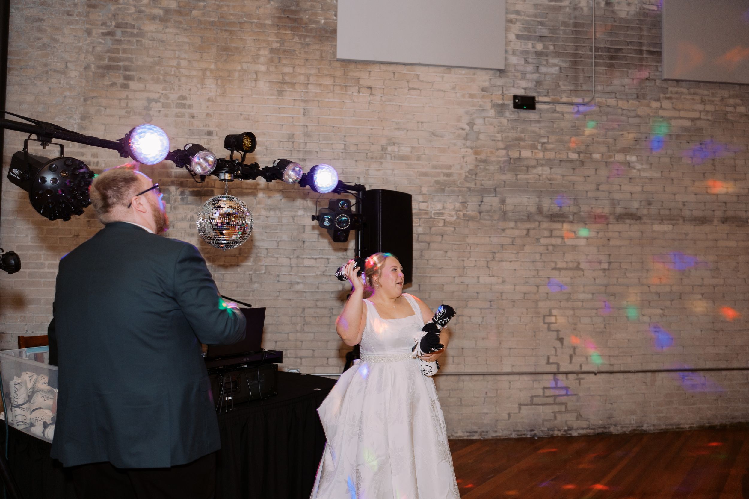 Couples dancing at a wedding reception in a rustic brick-walled venue with disco lights and decorations.