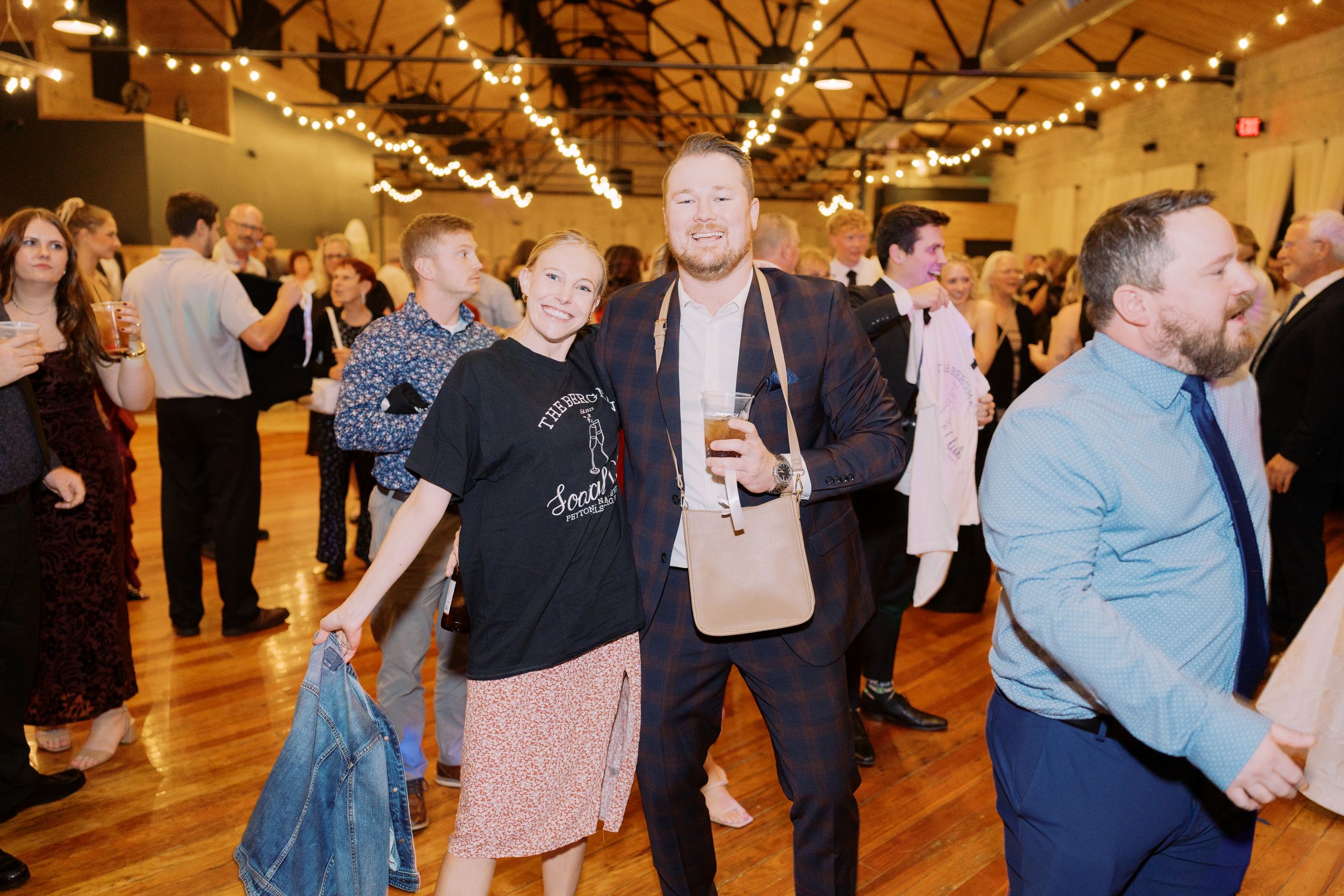 People enjoying a lively dance party in a rustic venue with wooden floors and string lights overhead.