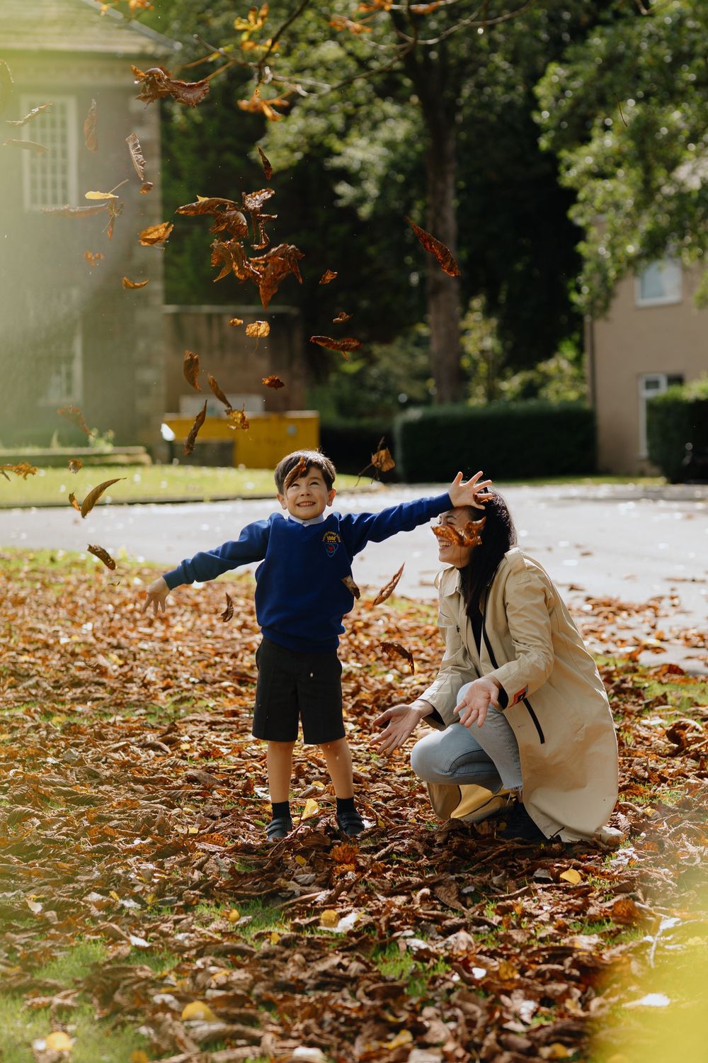 Couple playfully throws autumn leaves while sitting together on ground covered in fall foliage.