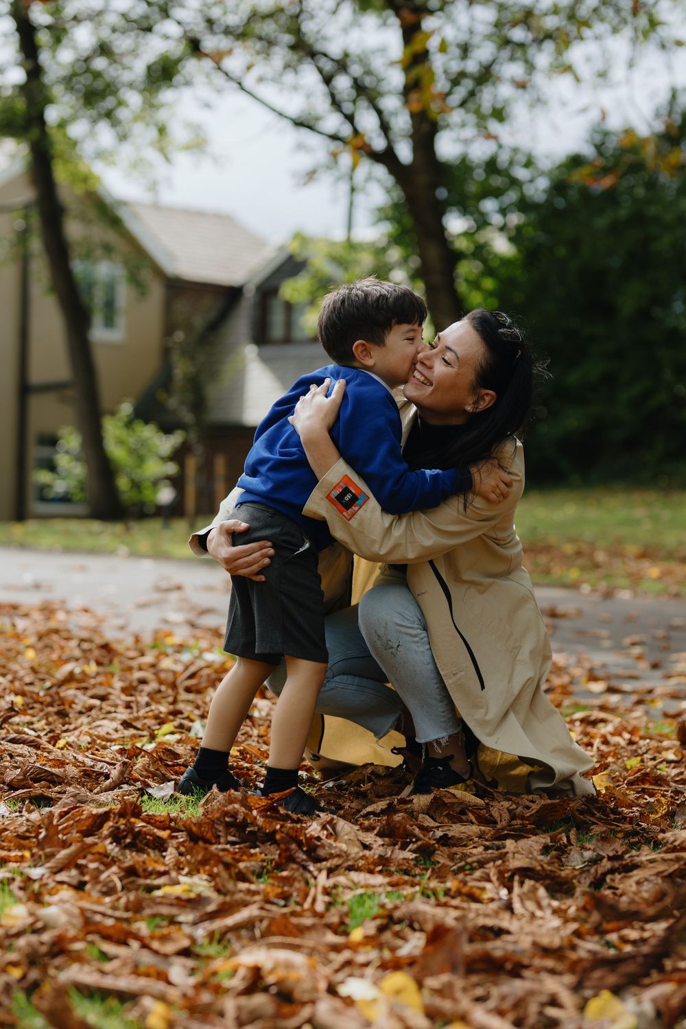A tender moment shared between parent and child playing together in fallen autumn leaves outside their home.