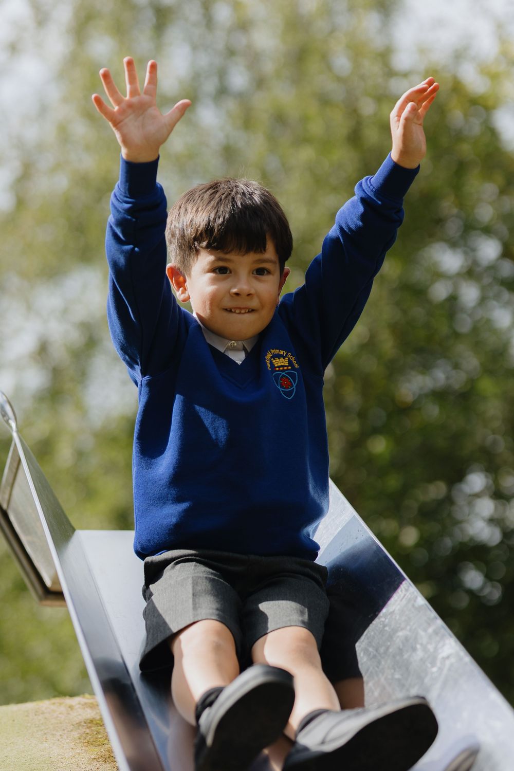 Young student in blue school uniform jumps joyfully on playground equipment outdoors.