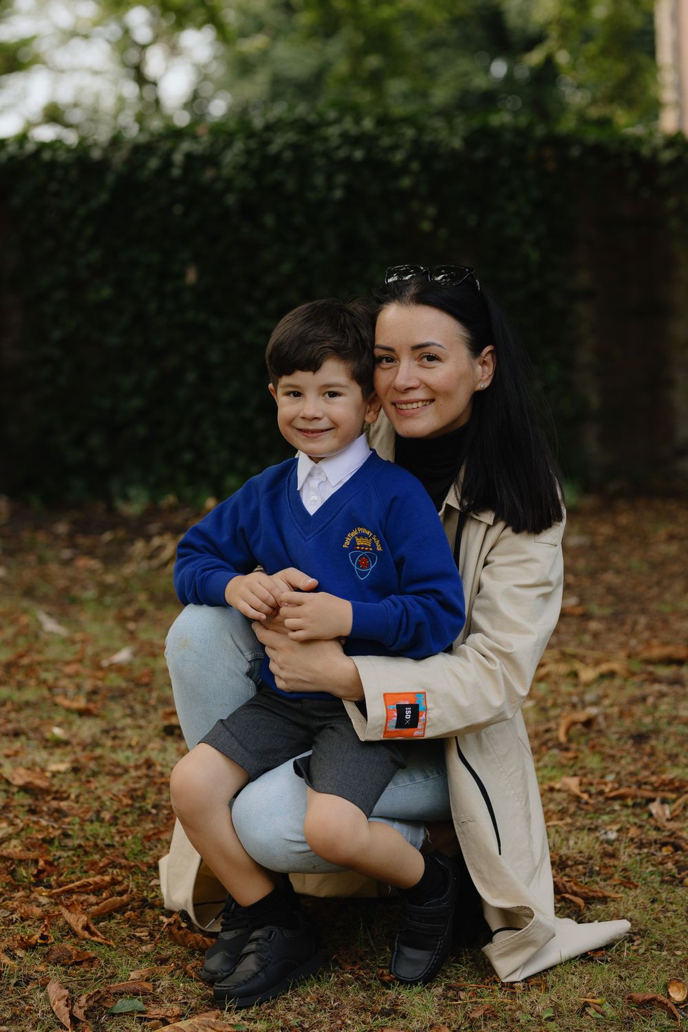 Student in blue school uniform sits with adult on autumn ground covered with fallen leaves.