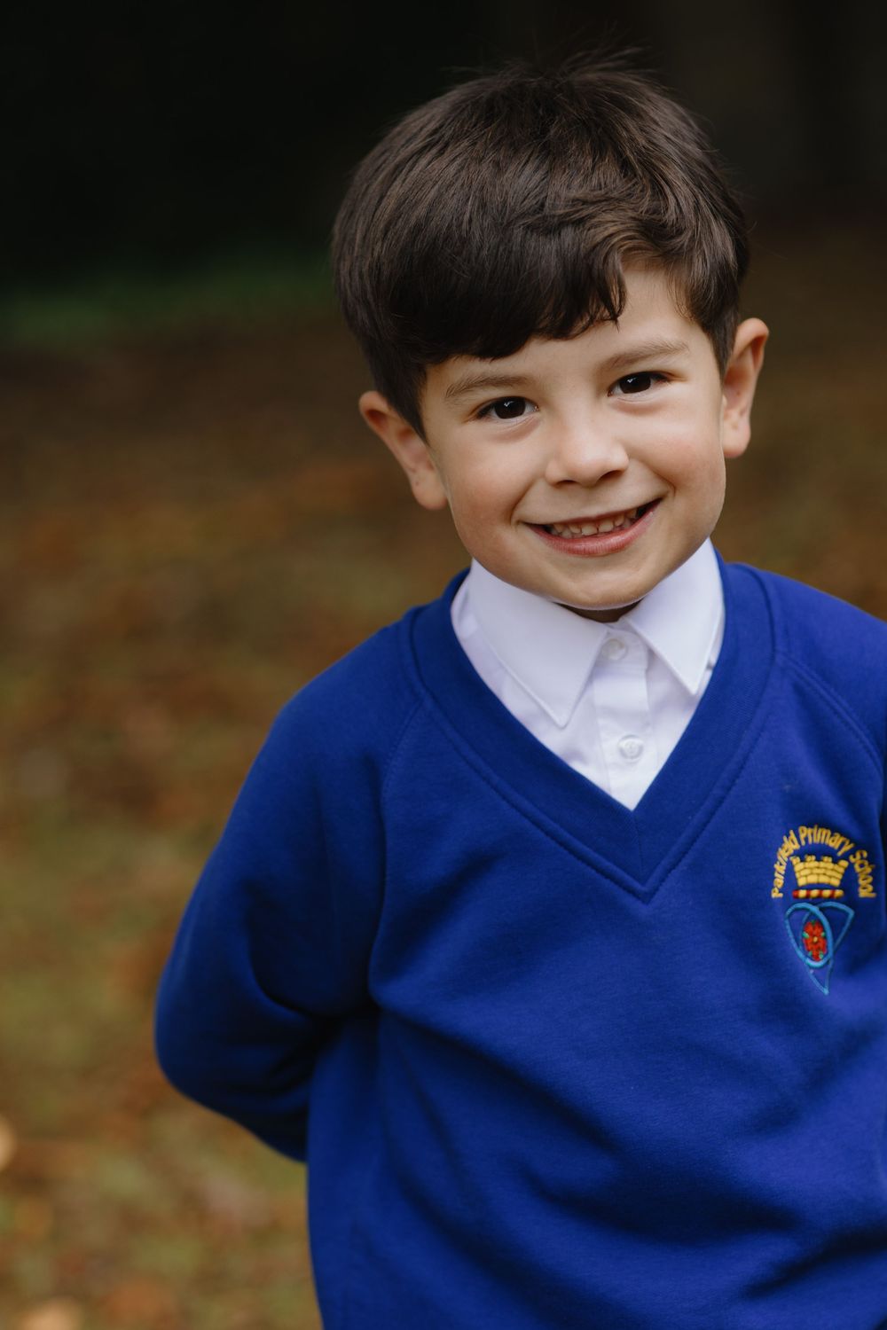 A child in a blue school uniform sweater and white collar smiles brightly in a series of outdoor portrait photos.