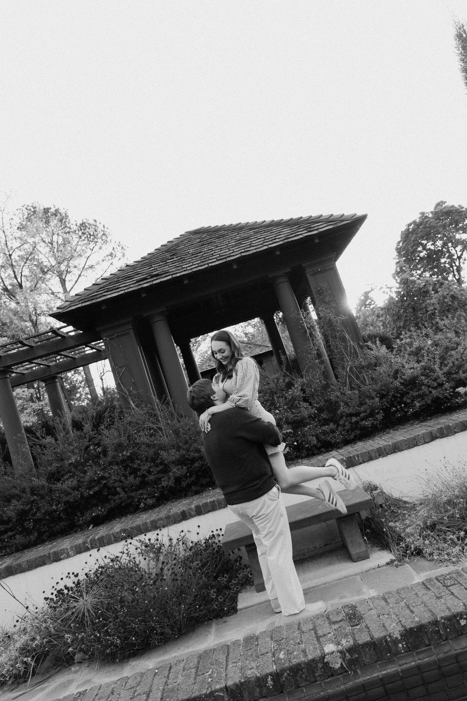 A sequence of three black and white photos showing a martial artist performing a high spinning kick in an outdoor garden setting.