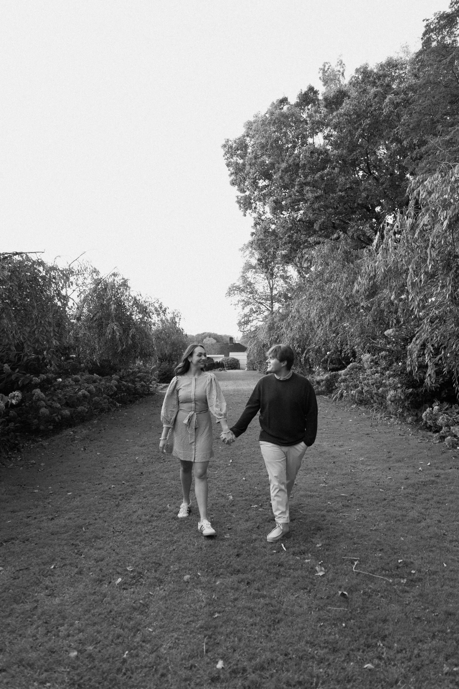 Two people walking together on a grassy hill path through trees in a black and white photograph.