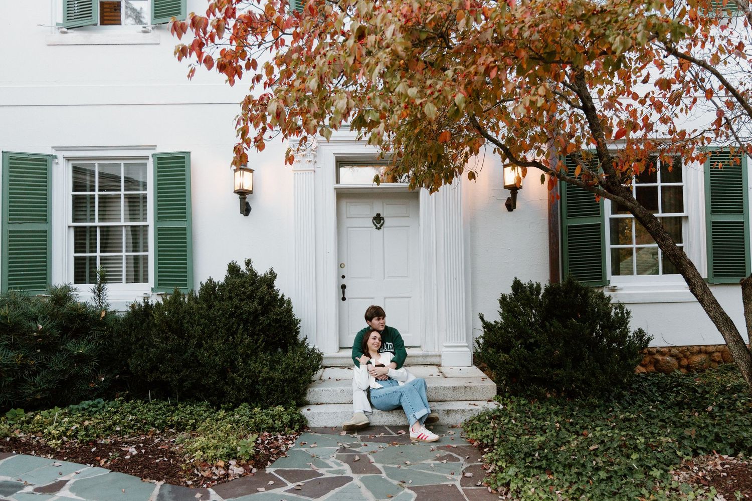 White colonial style house with green shutters and autumn foliage in front yard during fall season.