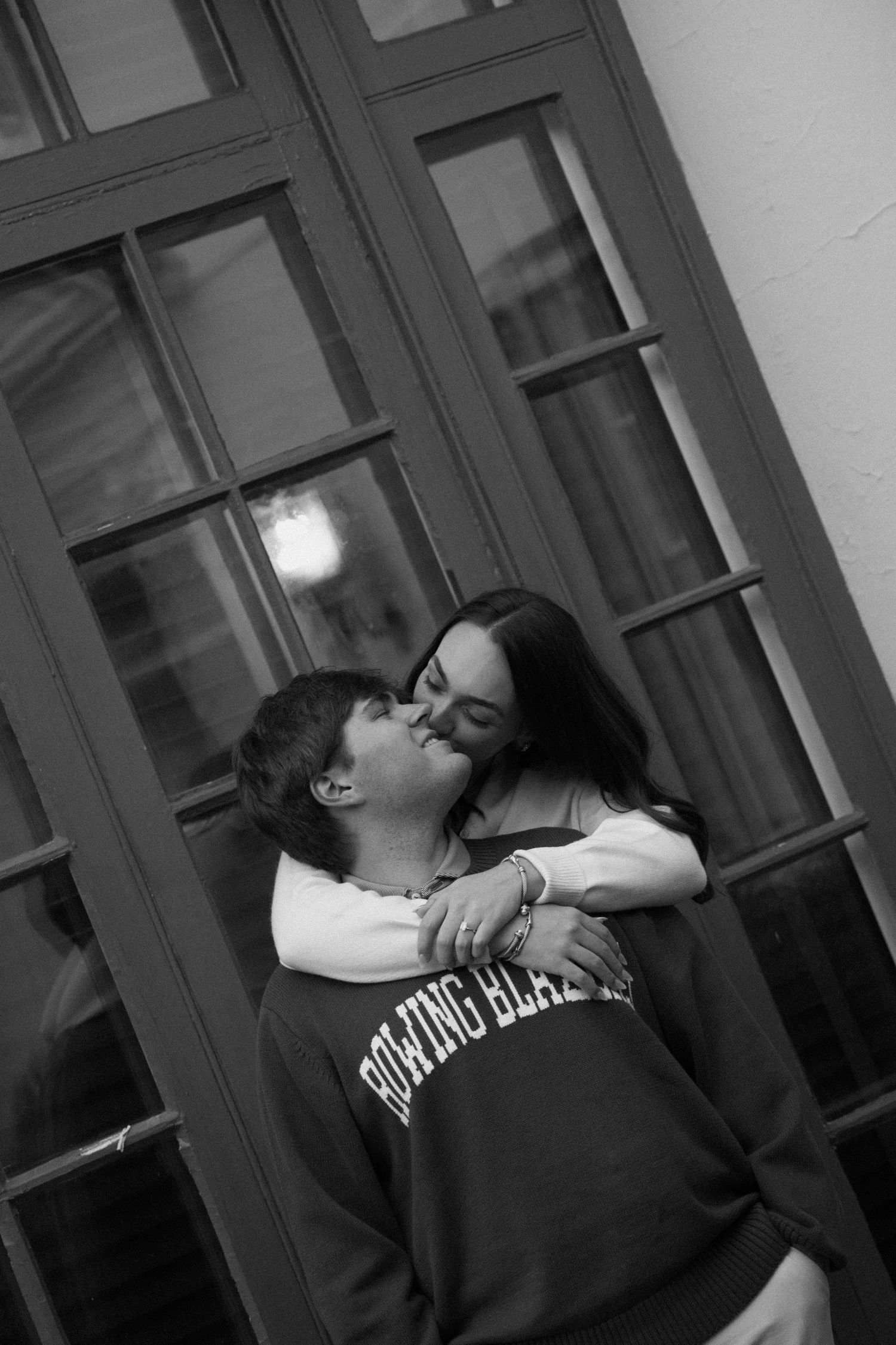 A romantic black and white photo of a couple embracing and kissing in front of a windowed door.