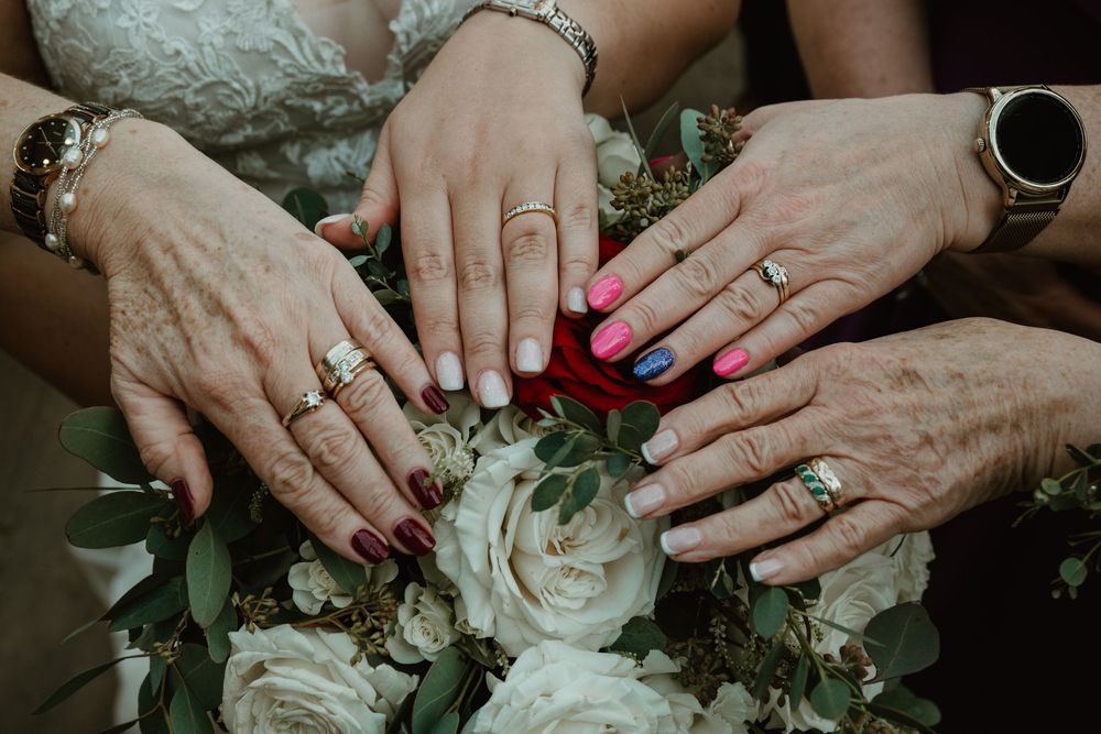 Close-up view of hands with wedding rings gently touching delicate white flowers and greenery in an elegant arrangement.