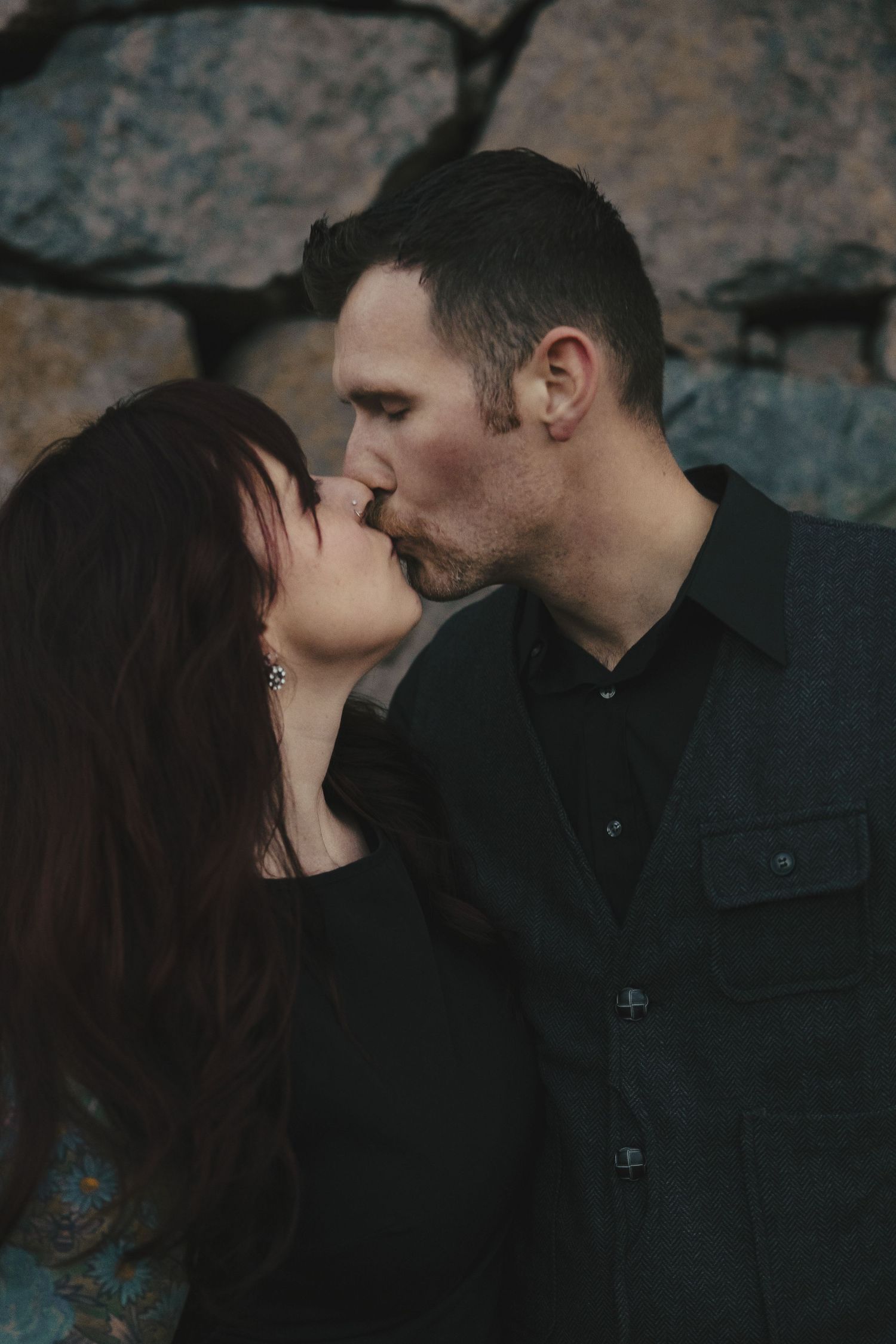 A romantic couple shares an intimate kiss in a dimly lit cave-like setting with textured stone walls in the background.