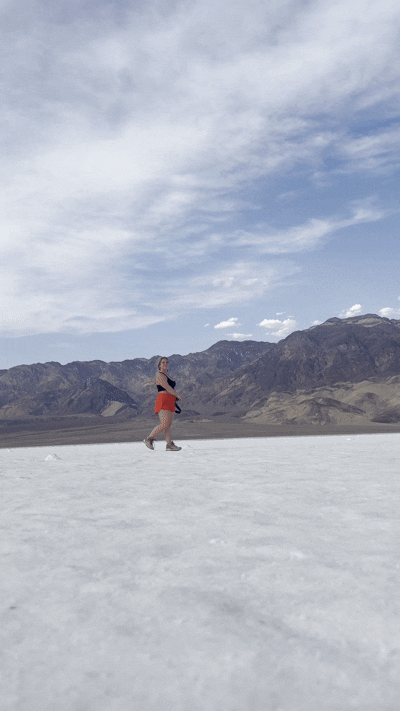 Person jumping on vast white salt flats with rugged mountains and cloudy sky in the background.