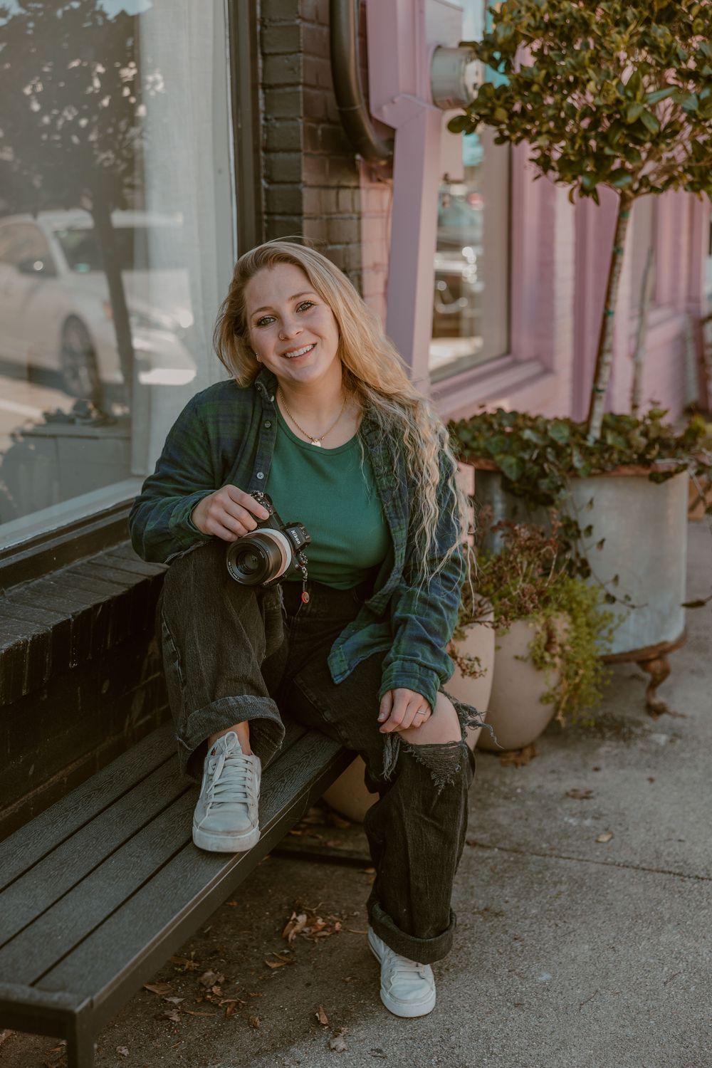A person in a green sweater poses casually on a wooden porch in an outdoor setting.