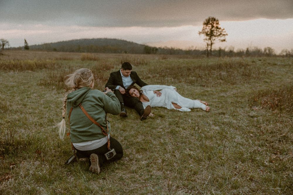 Two people in winter coats lay on a grassy hillside during an overcast day.