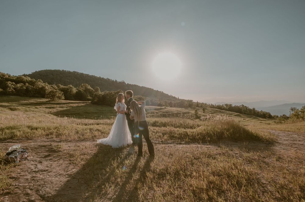 A couple walks along a scenic mountain trail during golden hour with rolling hills in the background.