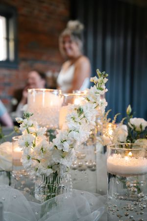 Elegant white floral centerpiece with candles and pearls at a wedding reception.