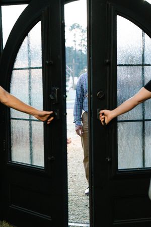 Two people open elegant black double doors with arched frosted glass panels outdoors.