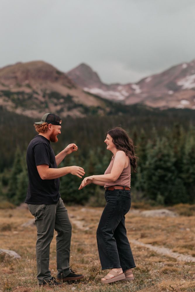 A laughing toddler in a plaid shirt stands outdoors against a scenic mountain landscape at sunset.