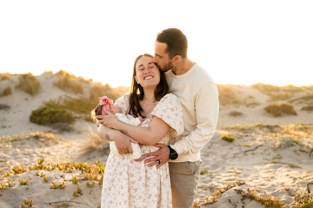Couple holding their newborn baby during a golden sunset beach newborn photoshoot in Ventura, captured by Ventura photographer